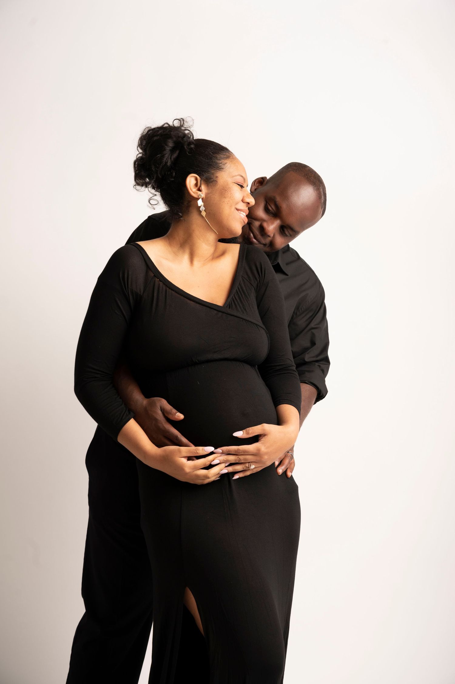 Maternity photoshoot featuring couple in black attire against white background showing tender moments.