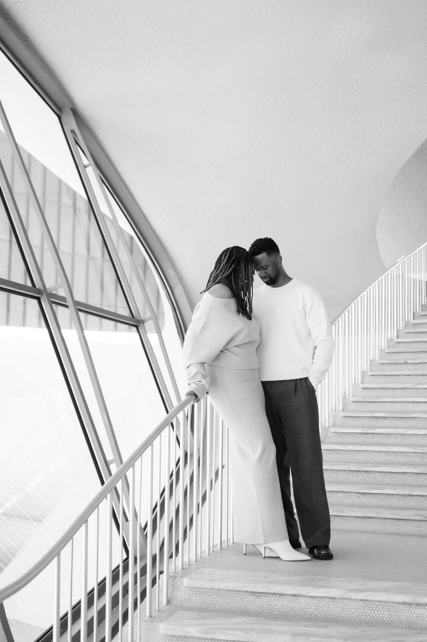 A couple ascending a modern white staircase in an architectural setting.