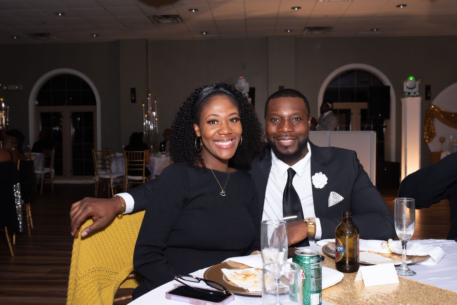 A smiling couple dressed in elegant black attire poses together at a formal banquet event.