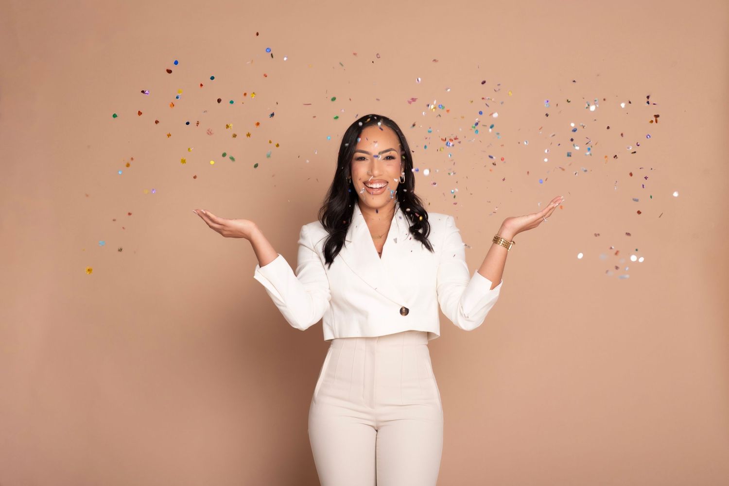 Celebratory portraits with confetti against peachy background in white professional attire.
