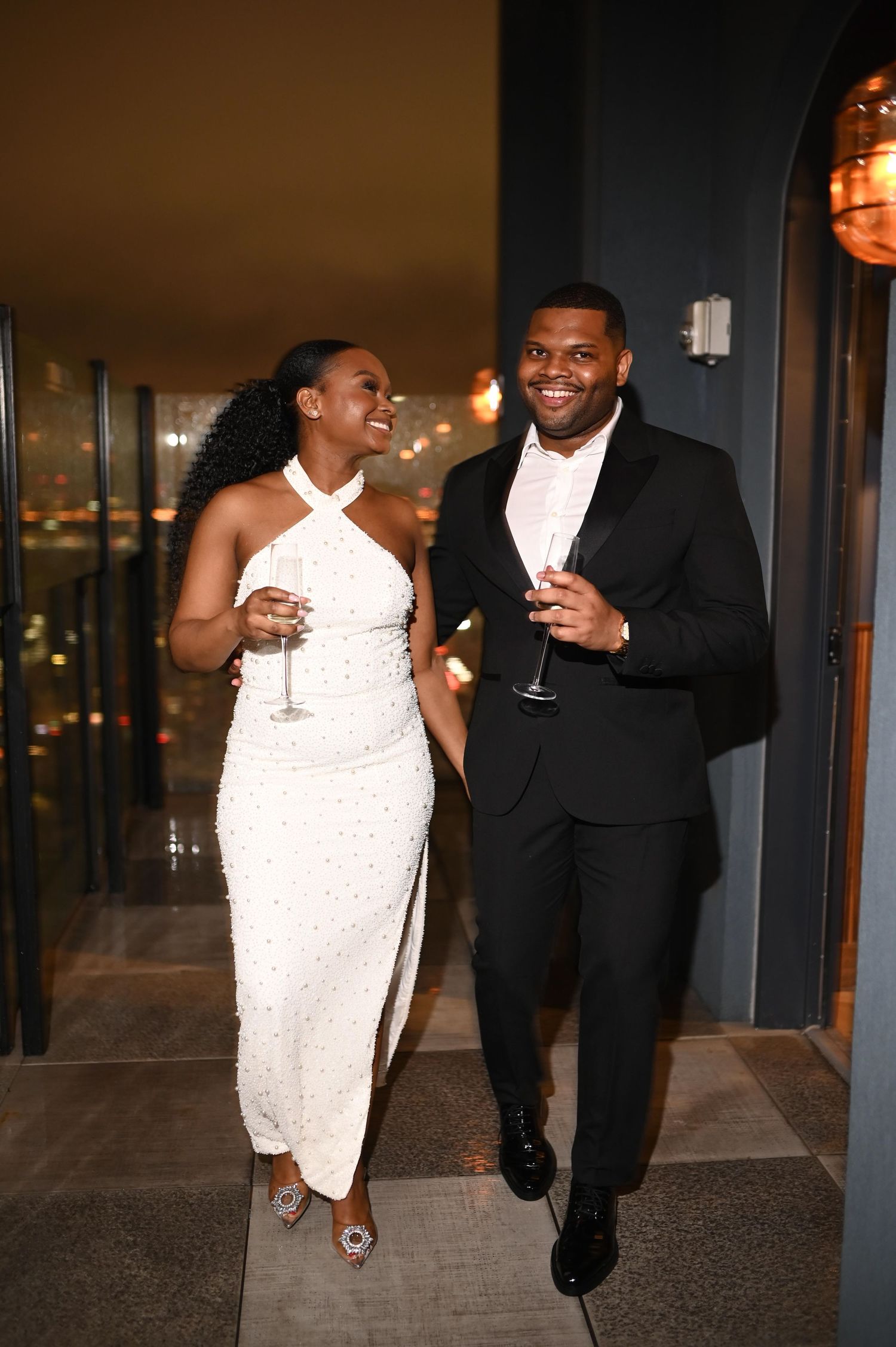 A couple in formal attire enjoying drinks and laughter at an evening event.