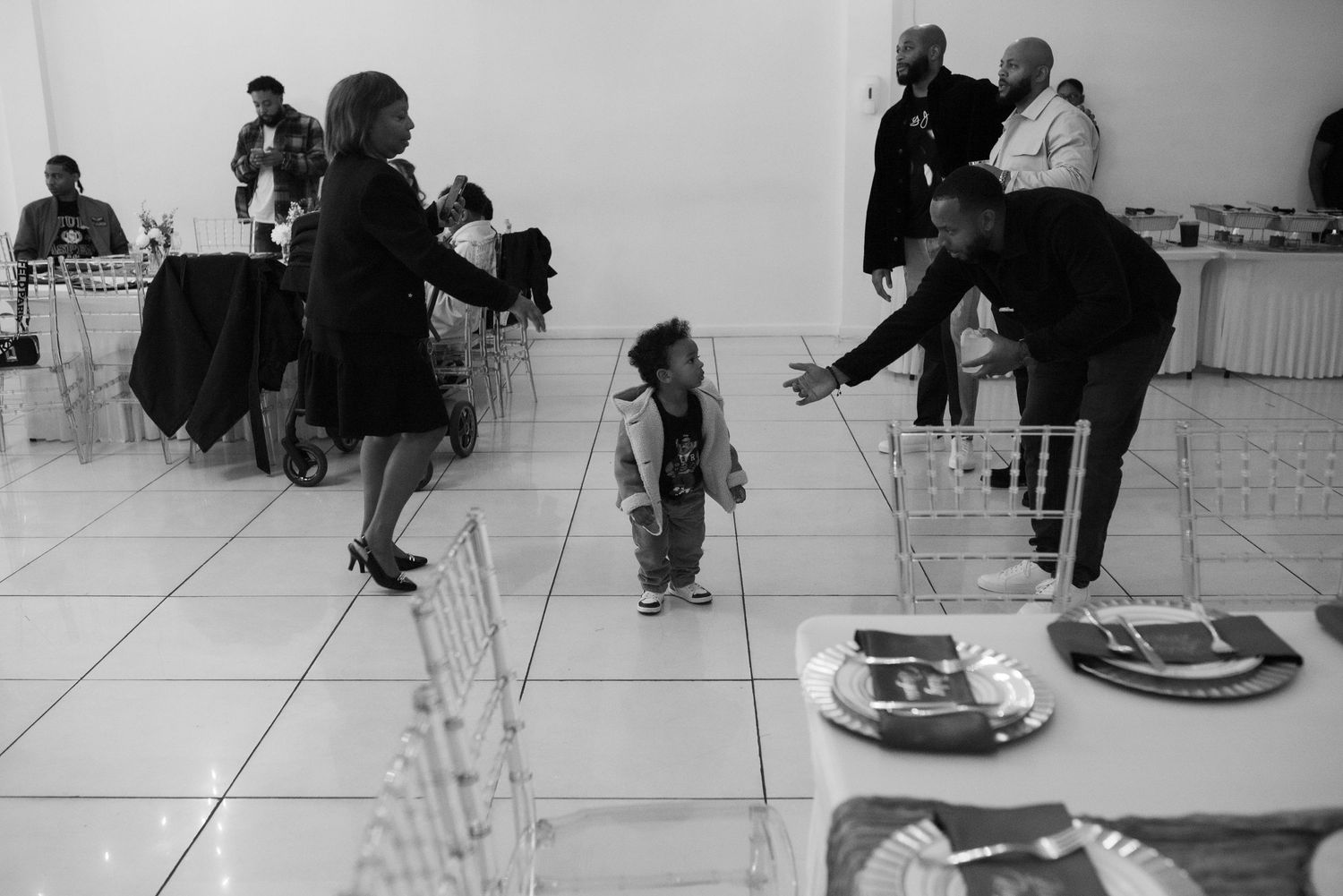 Black and white photo of adults and a small child at an indoor social gathering with elegant table settings.