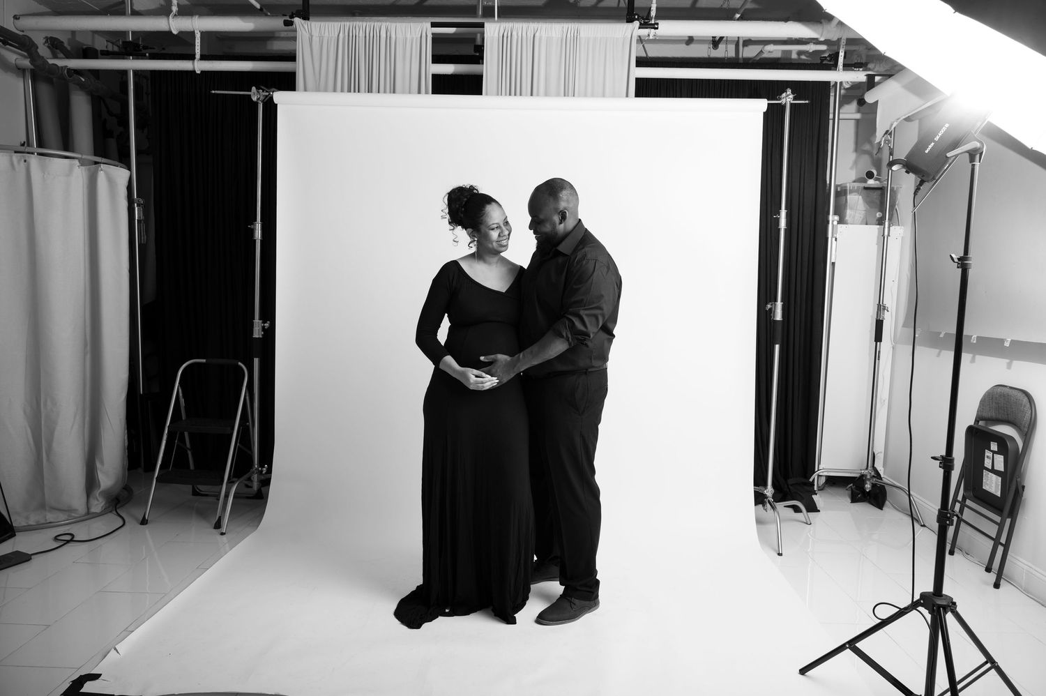 Behind-the-scenes photography session in a white studio with photographers and maternity couple