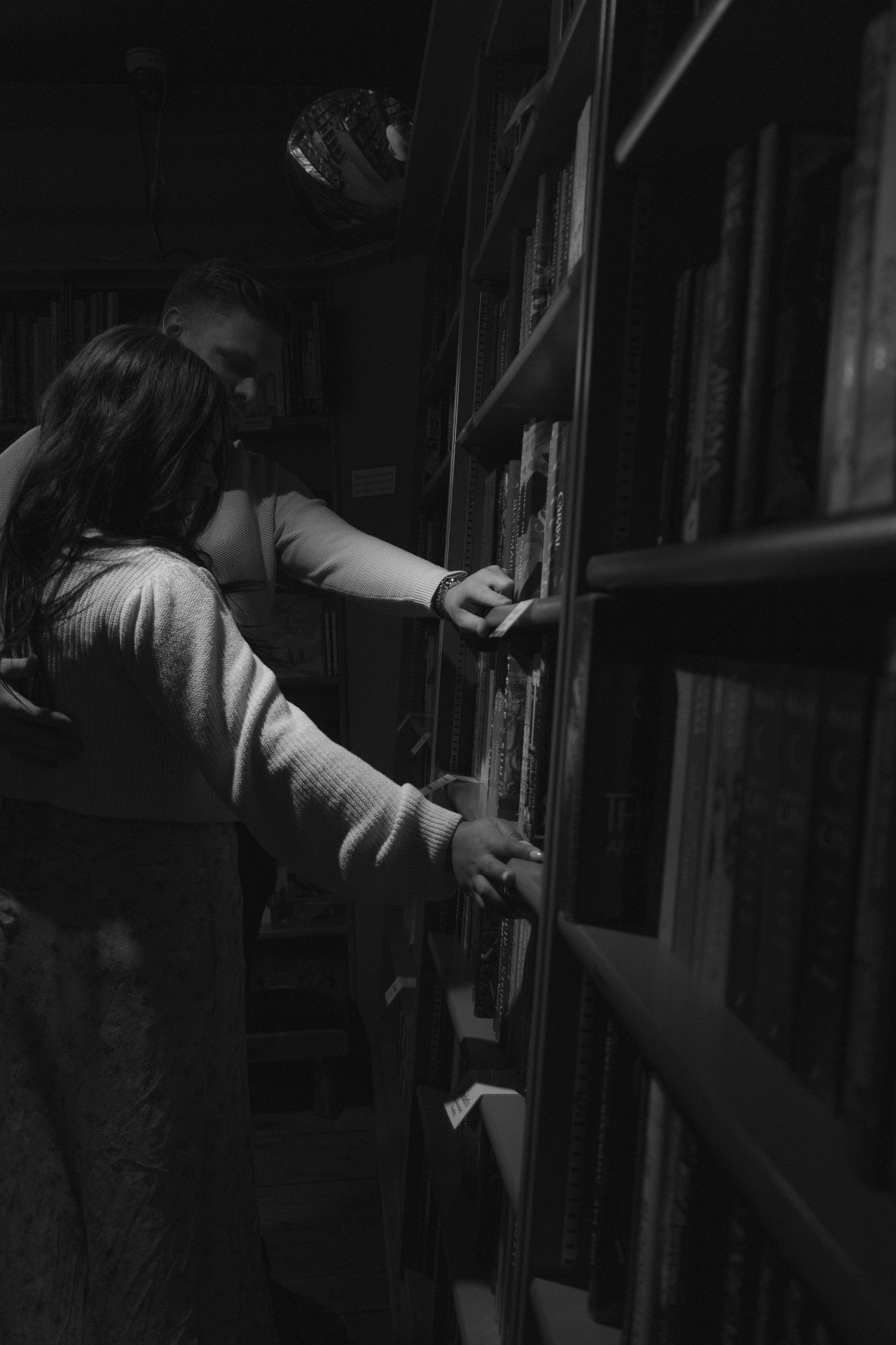 Black and white photo of a couple in a bookstore, hands on the bookcase. Nostalgic, film inspired