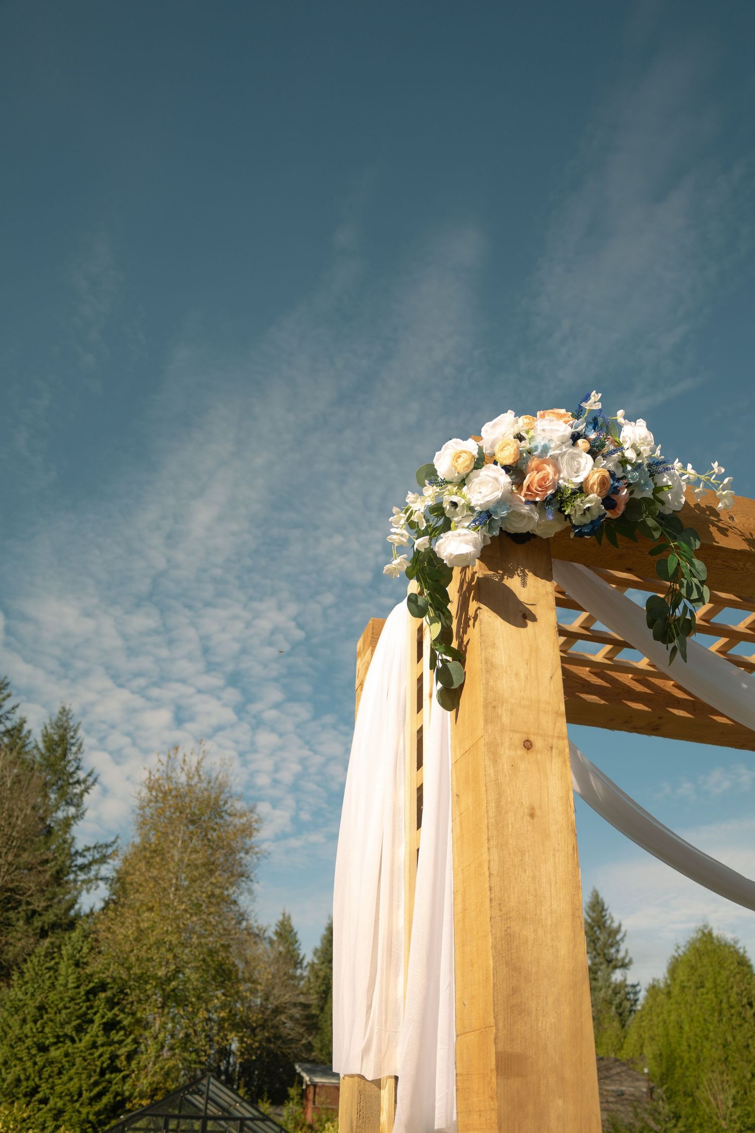 Wedding arch against a blue sky, flowers lining the arch. Cinematic couples, art inspired photography