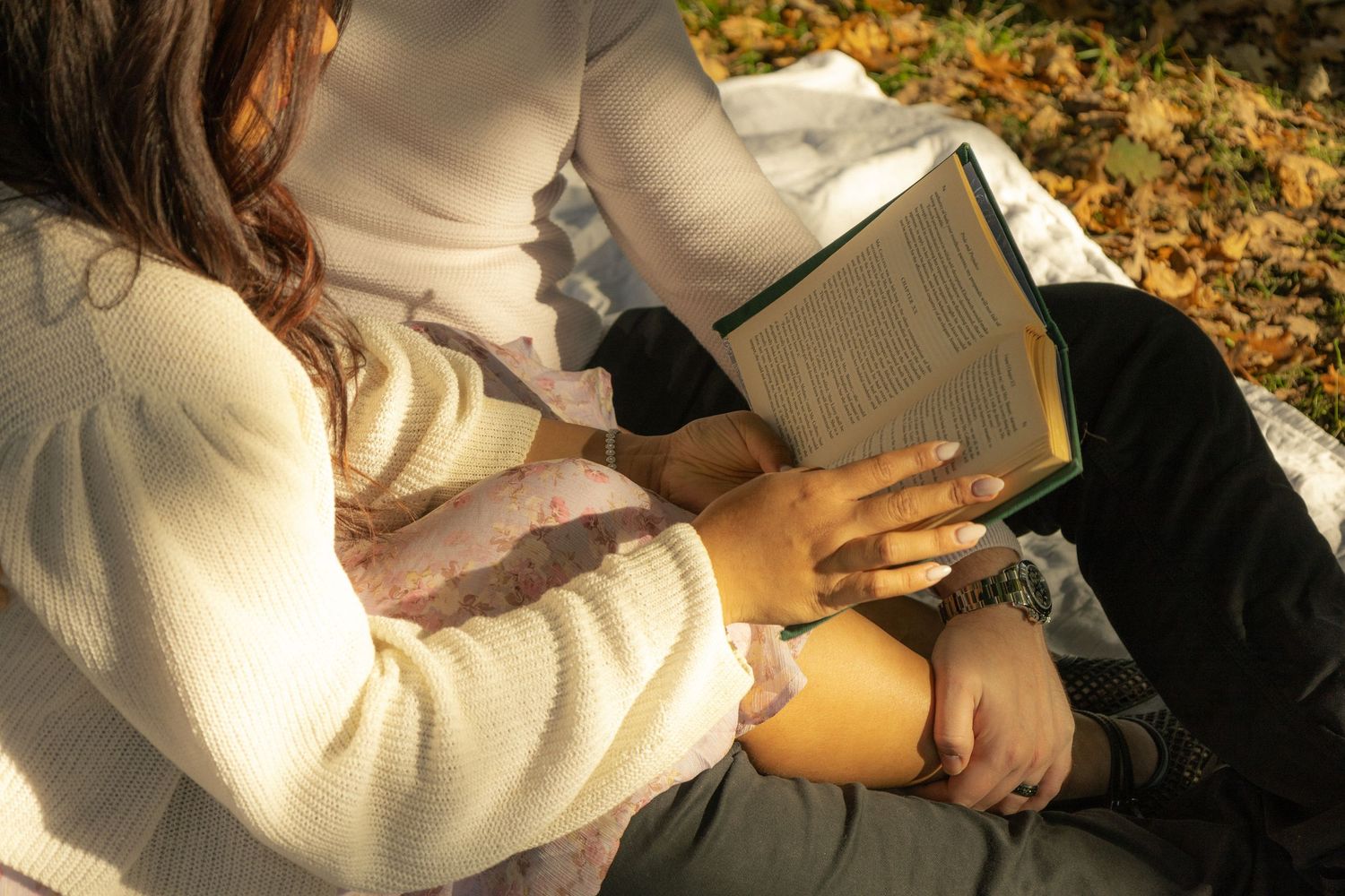 Couple seated together on a blanket in the grass, reading a book together. Cinematic photography style