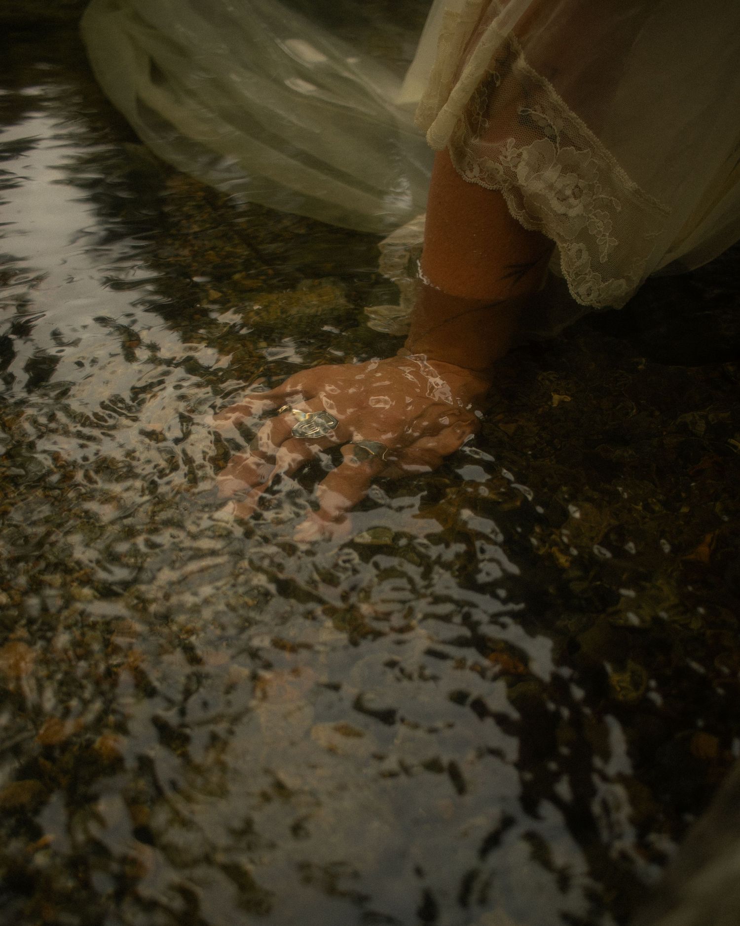 Documentary style photo of woman's hand beneath the water in a stream