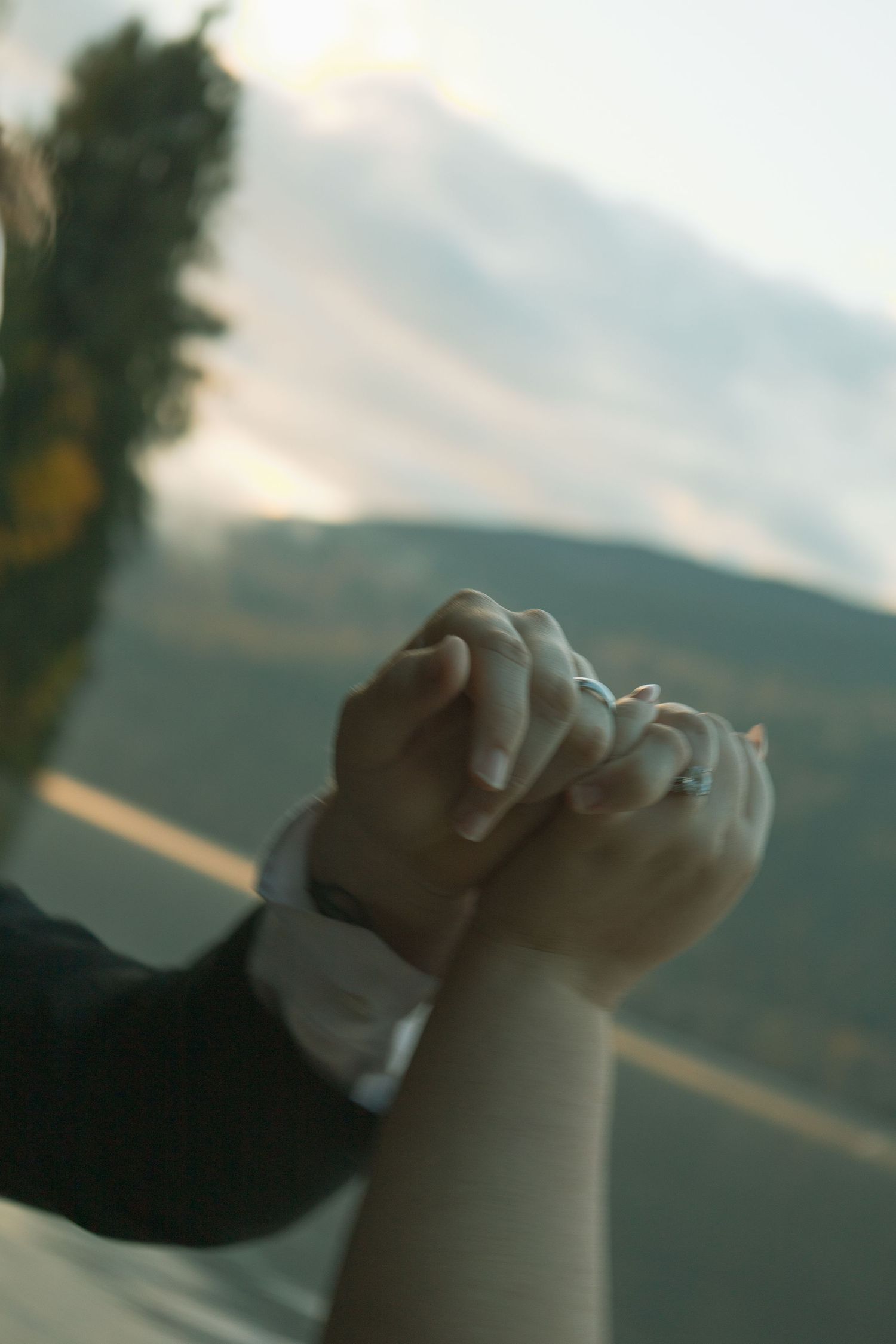 Couples hands are held together in a pinky promise against the sunset on the lake behind them