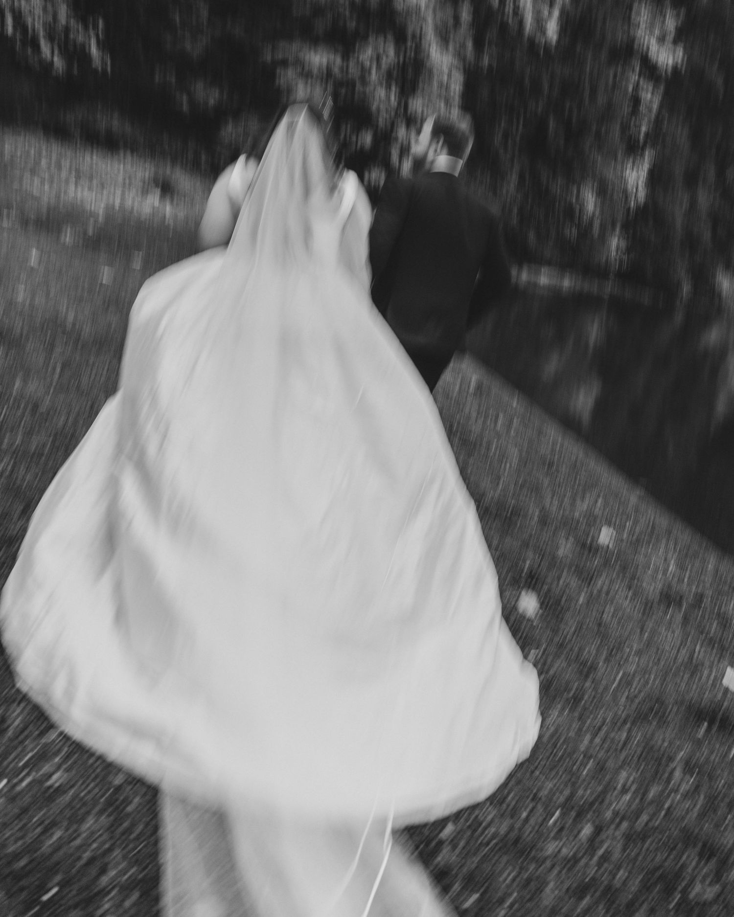 Black and white image of couple running alongside a lake, motion blur and grain used for a film inspired and nostalgic effect