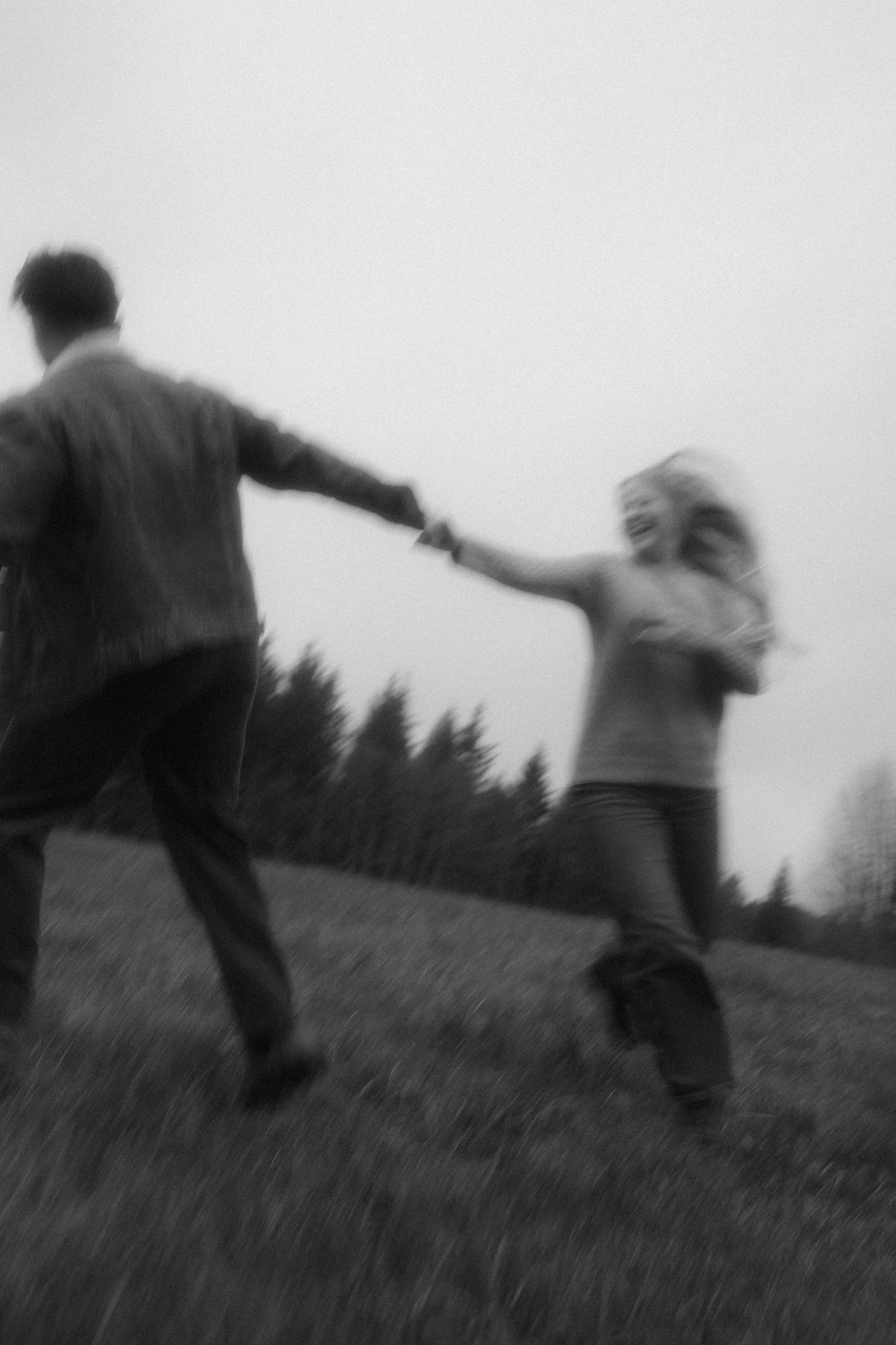Black and white photo, couple holding hands spinning and running through a field, motion blur, intentional grain, film photo inspired
