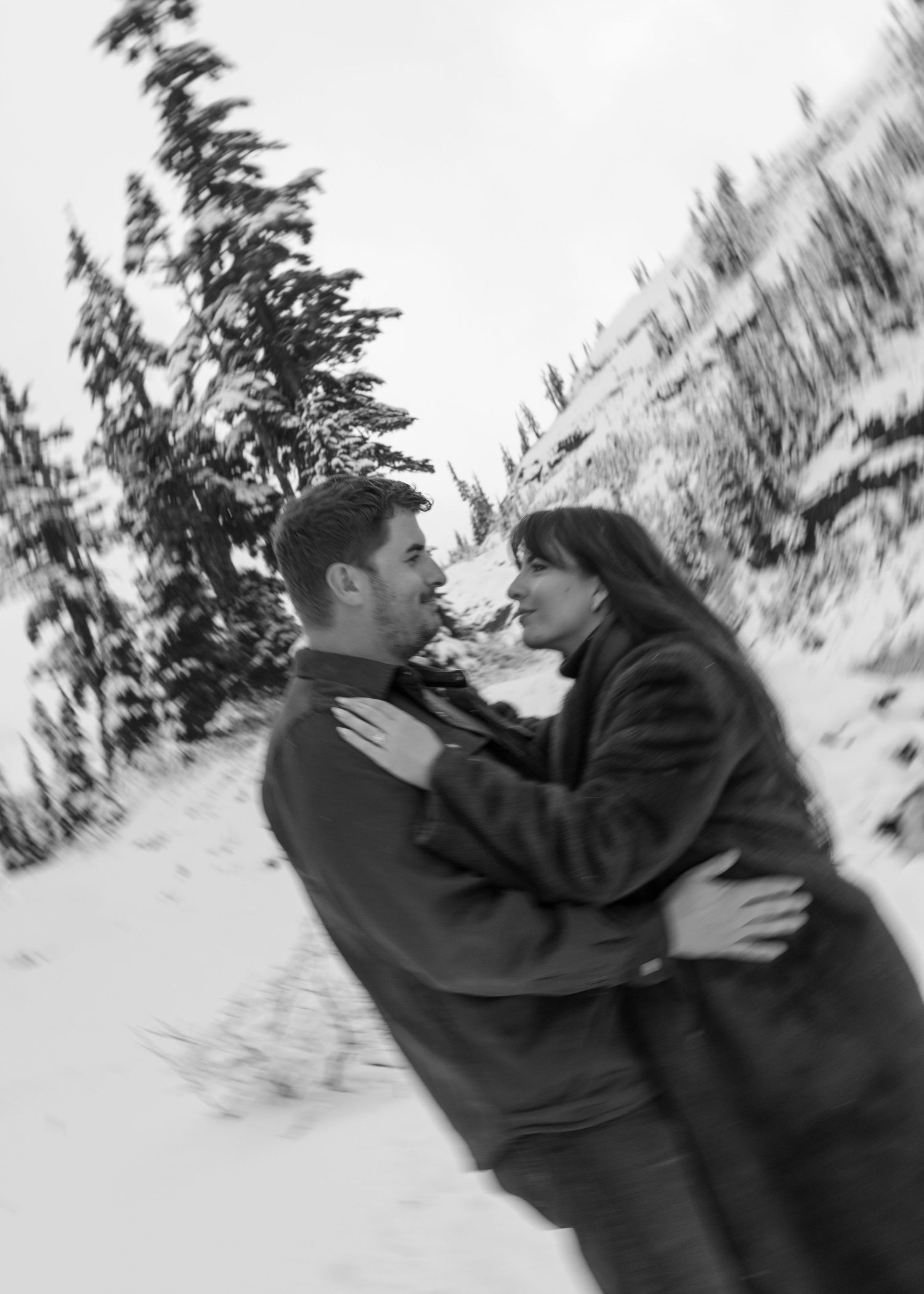 Black and white photo of couple embracing in the snow, motion blurred, grainy, film inspired, nostalgic vibes