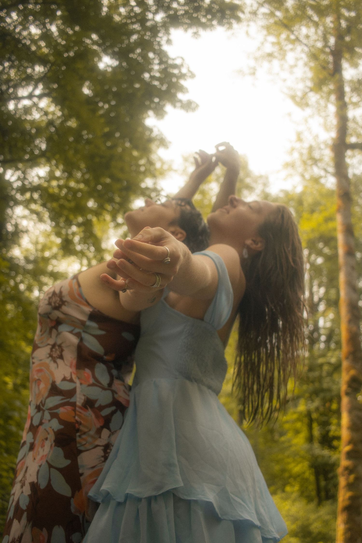 LGBTQ+ couple in nature, arms to the sky, viewer is looking at their joined hands leading up towards the sky. Documentary photography