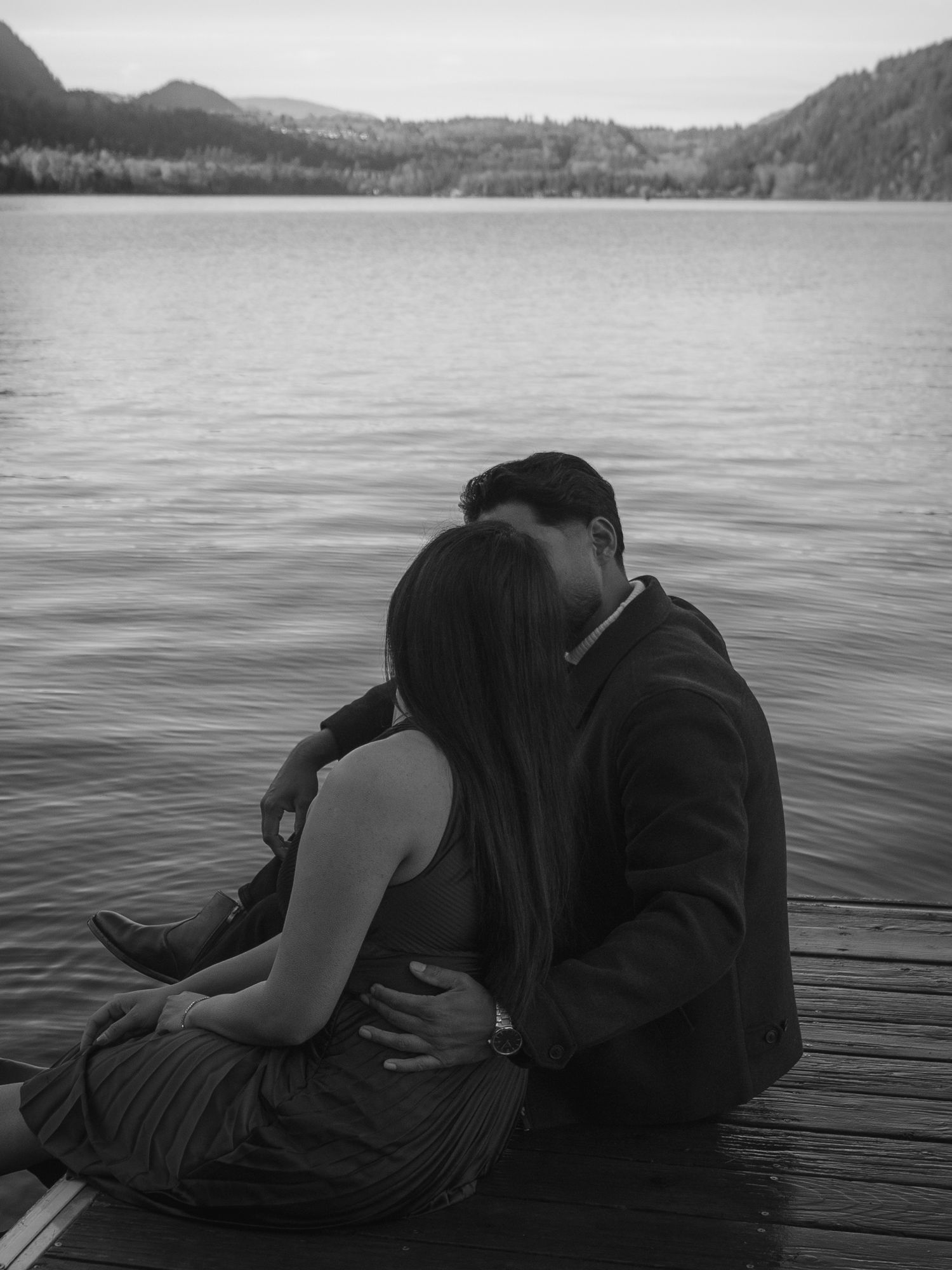 Couple sitting together on a dock, lake in the background, black and white image, intentional grain, nostalgic vibes