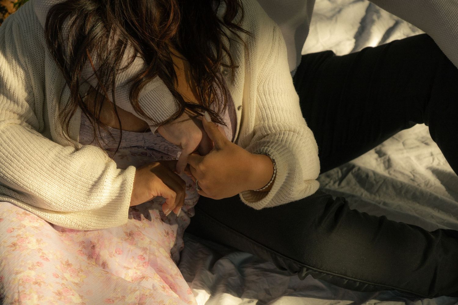 Couple seated together on a blanket in the grass. Close up shot of their hands together. Cinematic photography style