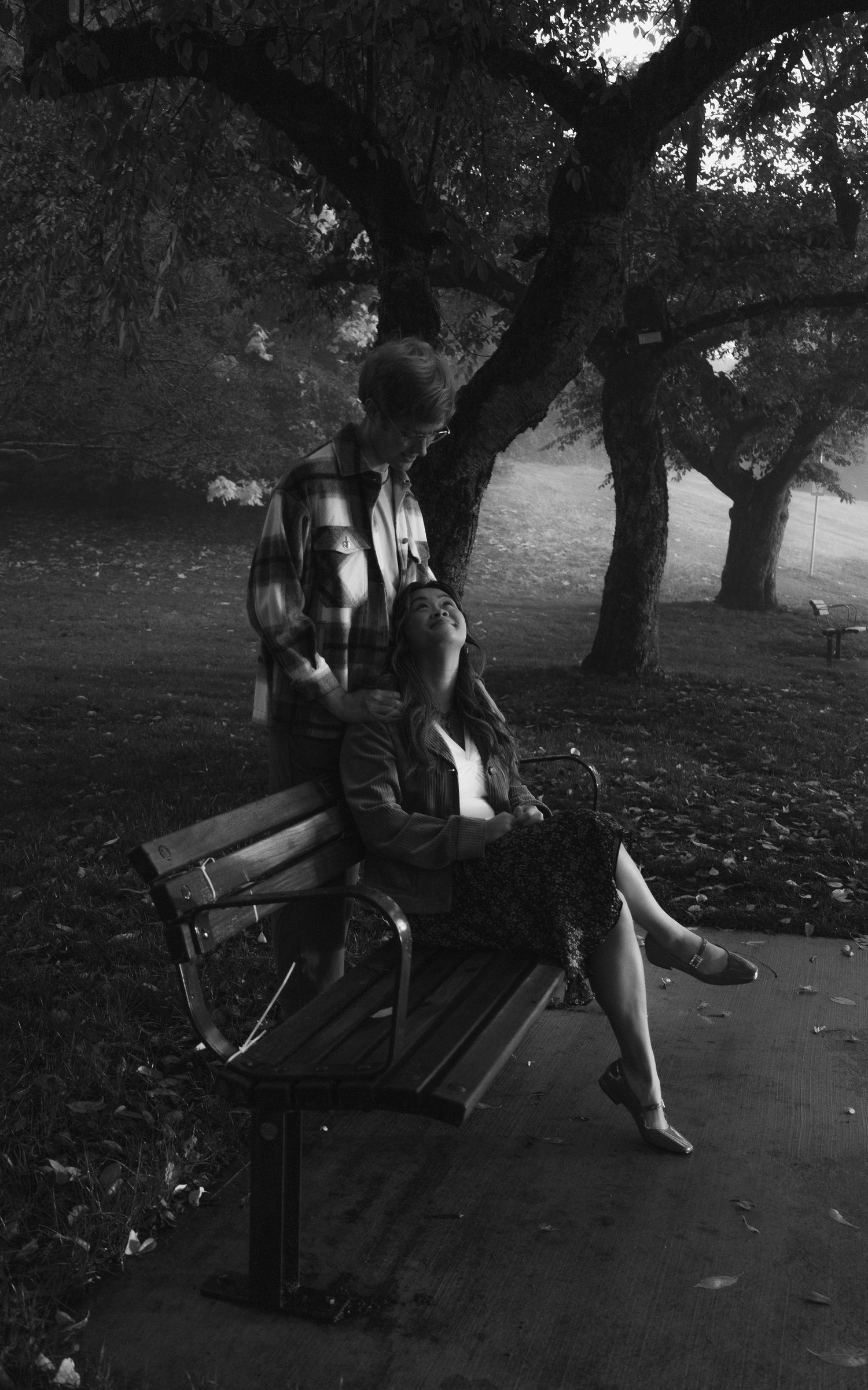 Black and white of couple outside, storytelling session,   woman sitting on a bench, looking up at man