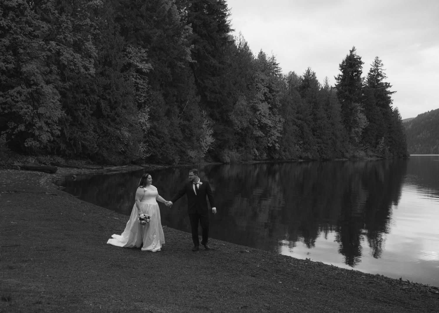 Black and white image of a couple walking alongside a lake holding hands, BC elopement photography