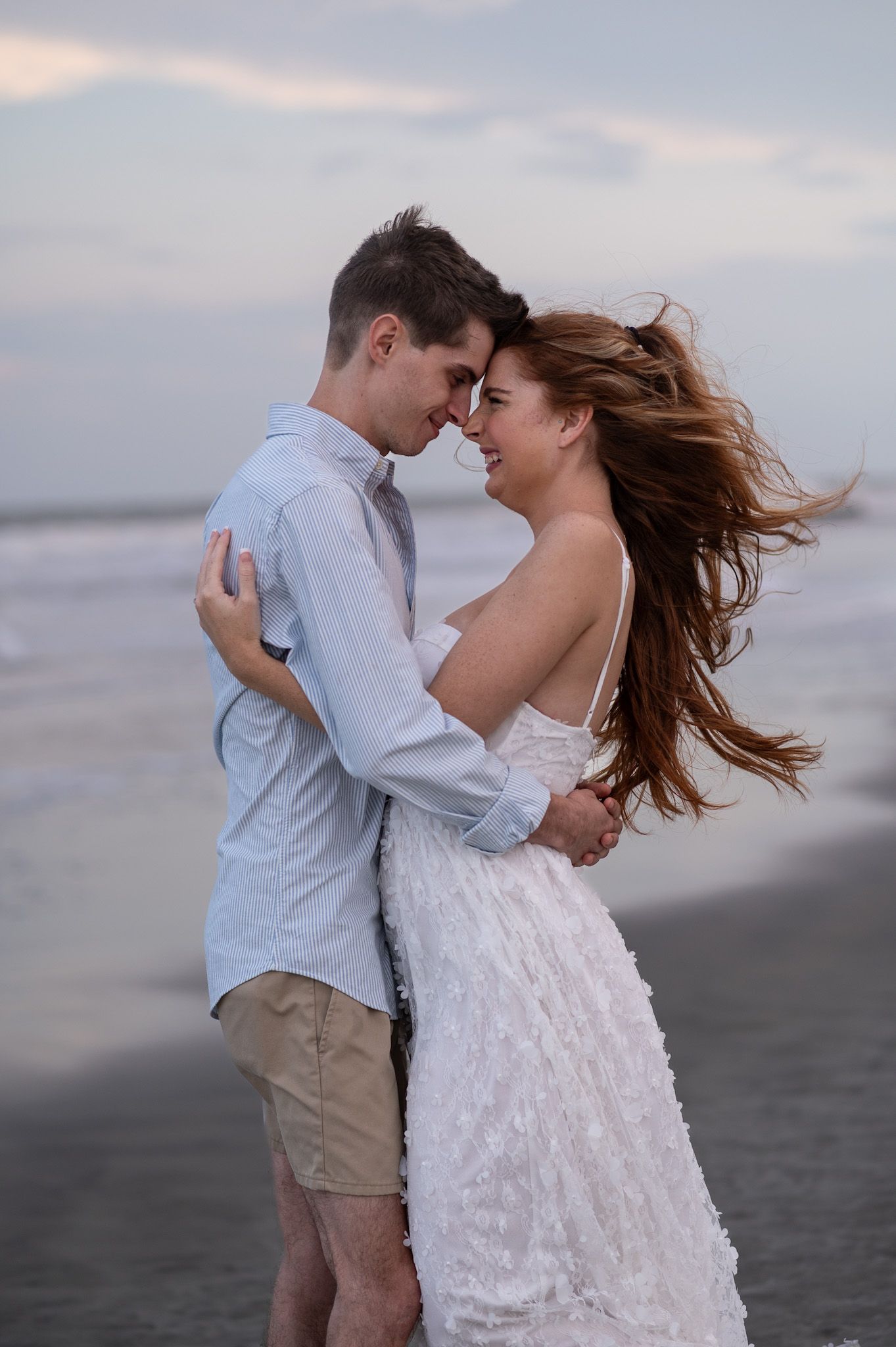 A romantic couple embraces and dances together on a cloudy beach at dusk.