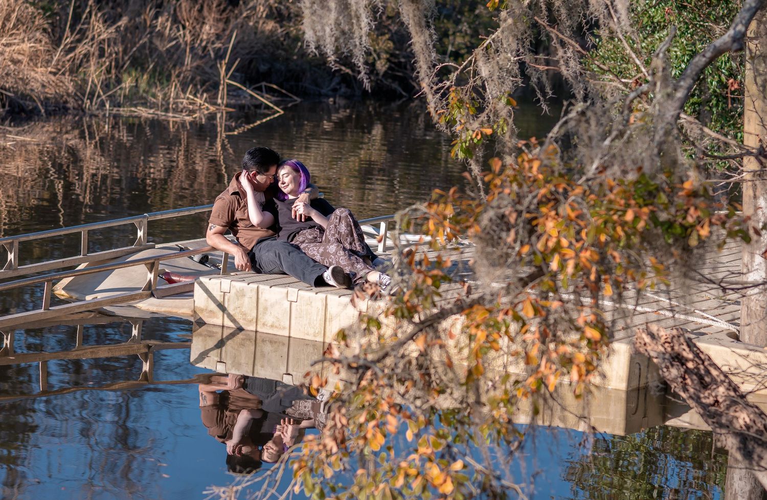 A wide documentary-style photo of a couple sitting by the water at the Ashley River Blue Trail in Summerville, SC, with sun-drenched docks