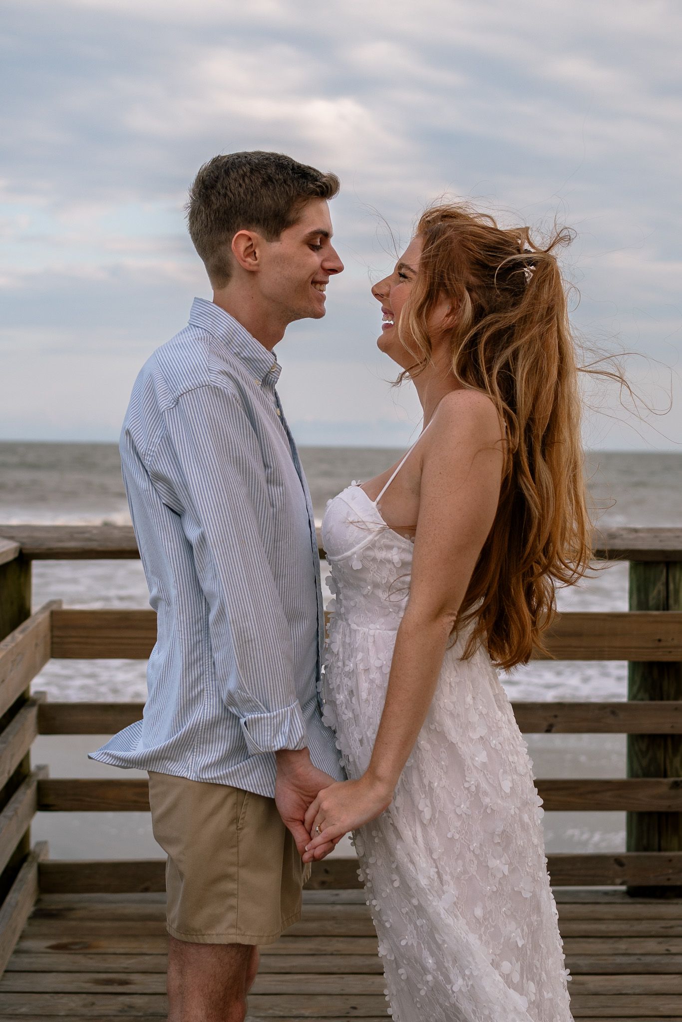 A romantic couple shares intimate moments on a wooden boardwalk overlooking the ocean at sunset.