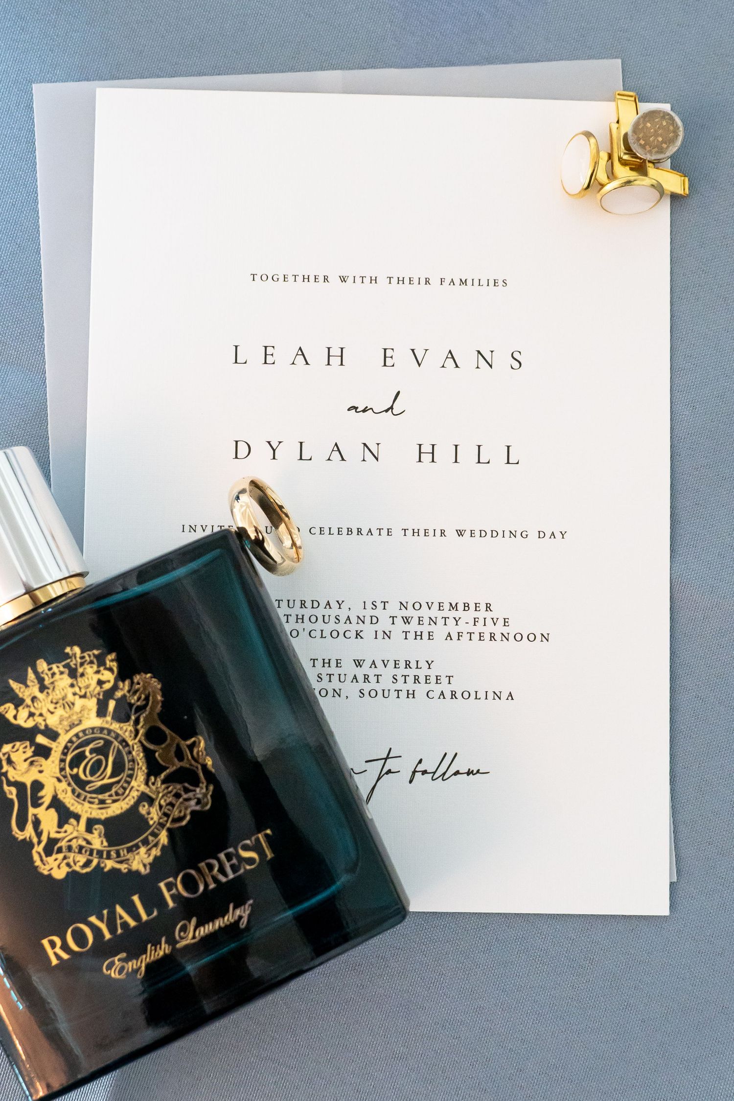 Elegant wedding invitation suite with gold accents and perfume bottles on blue background.