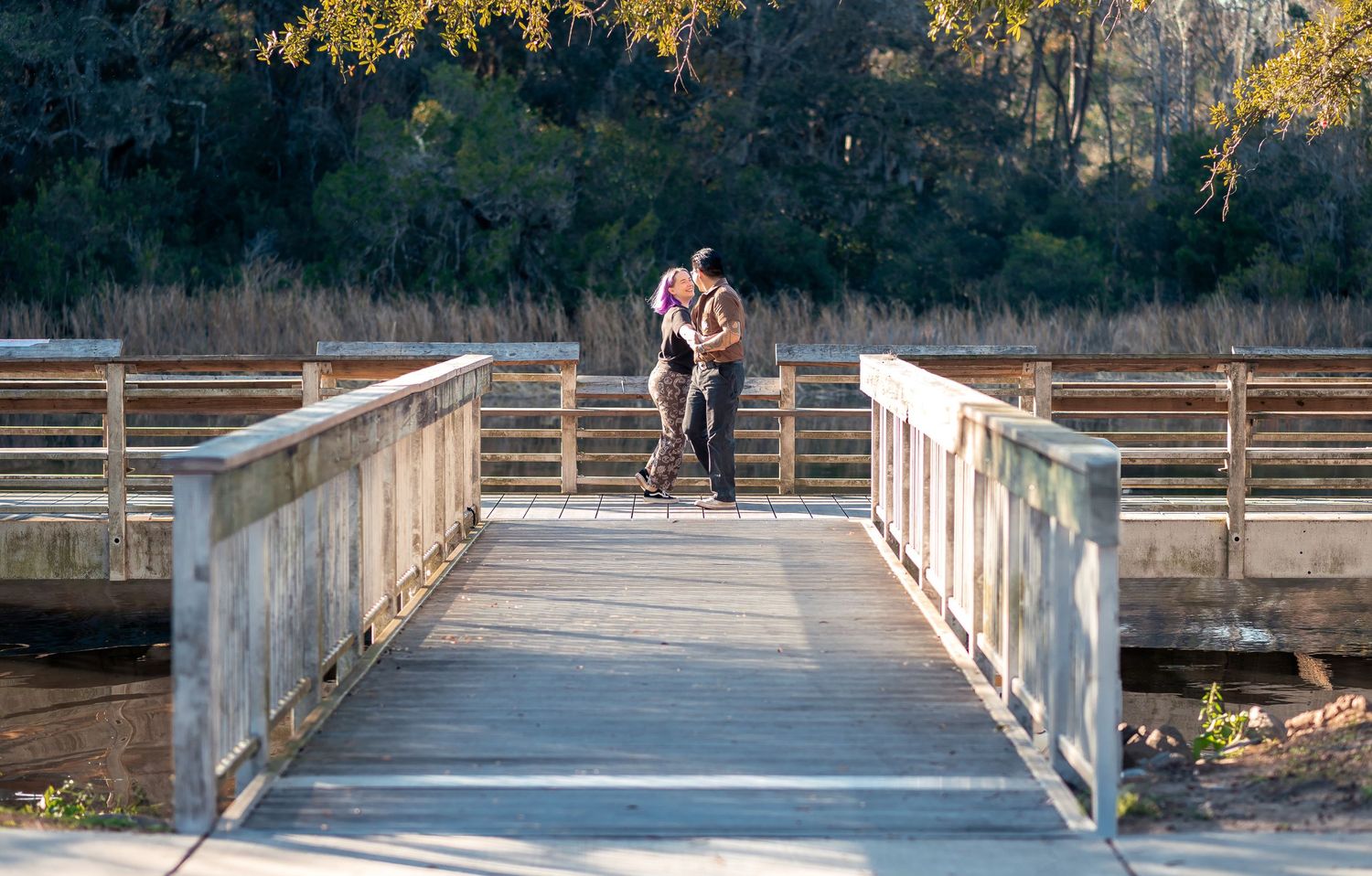 A wide documentary-style photo of a couple dancing by the water at the Ashley River Blue Trail in Summerville, SC, with sun-drenched docks