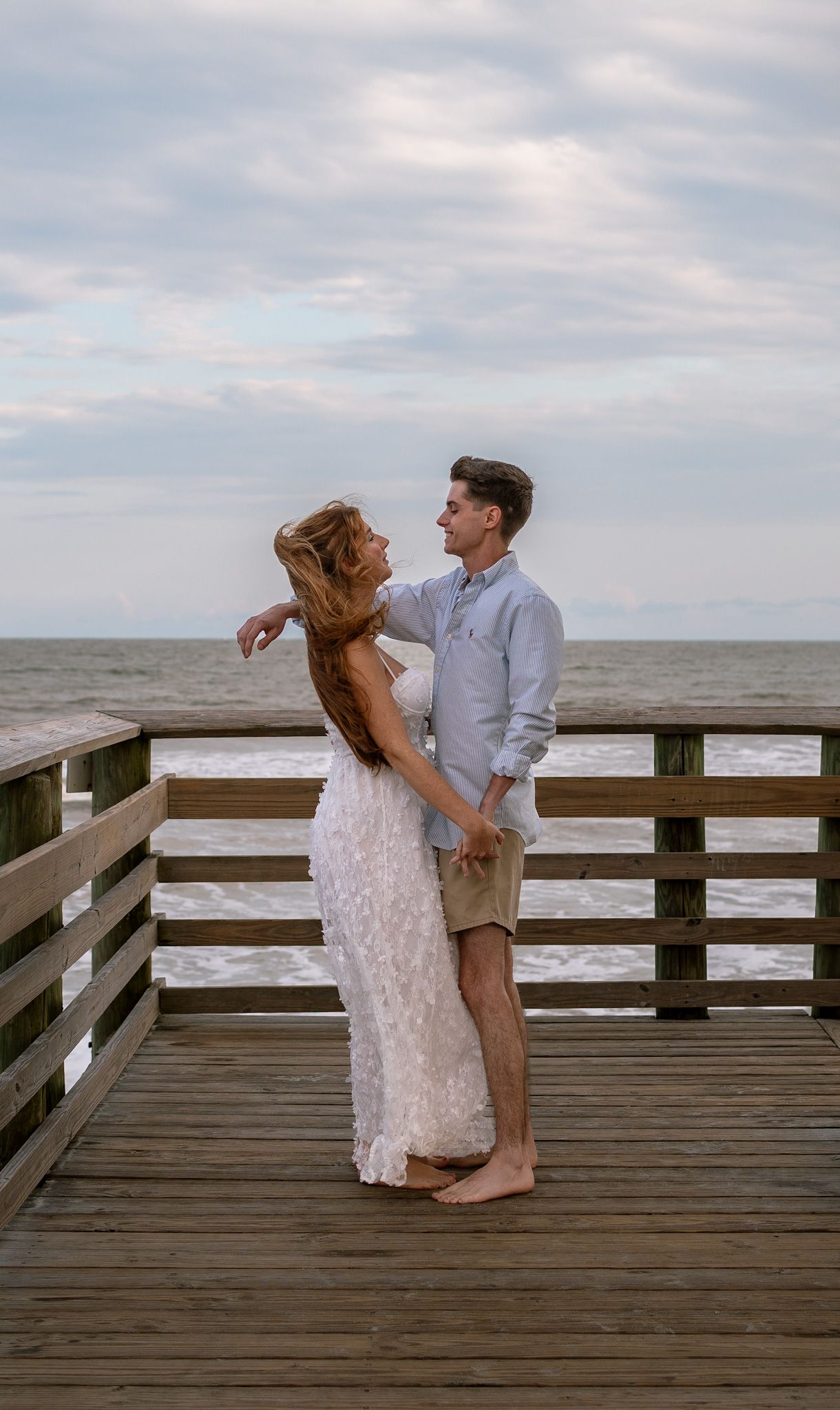 A couple shares a romantic moment on a wooden pier overlooking the ocean at dusk.