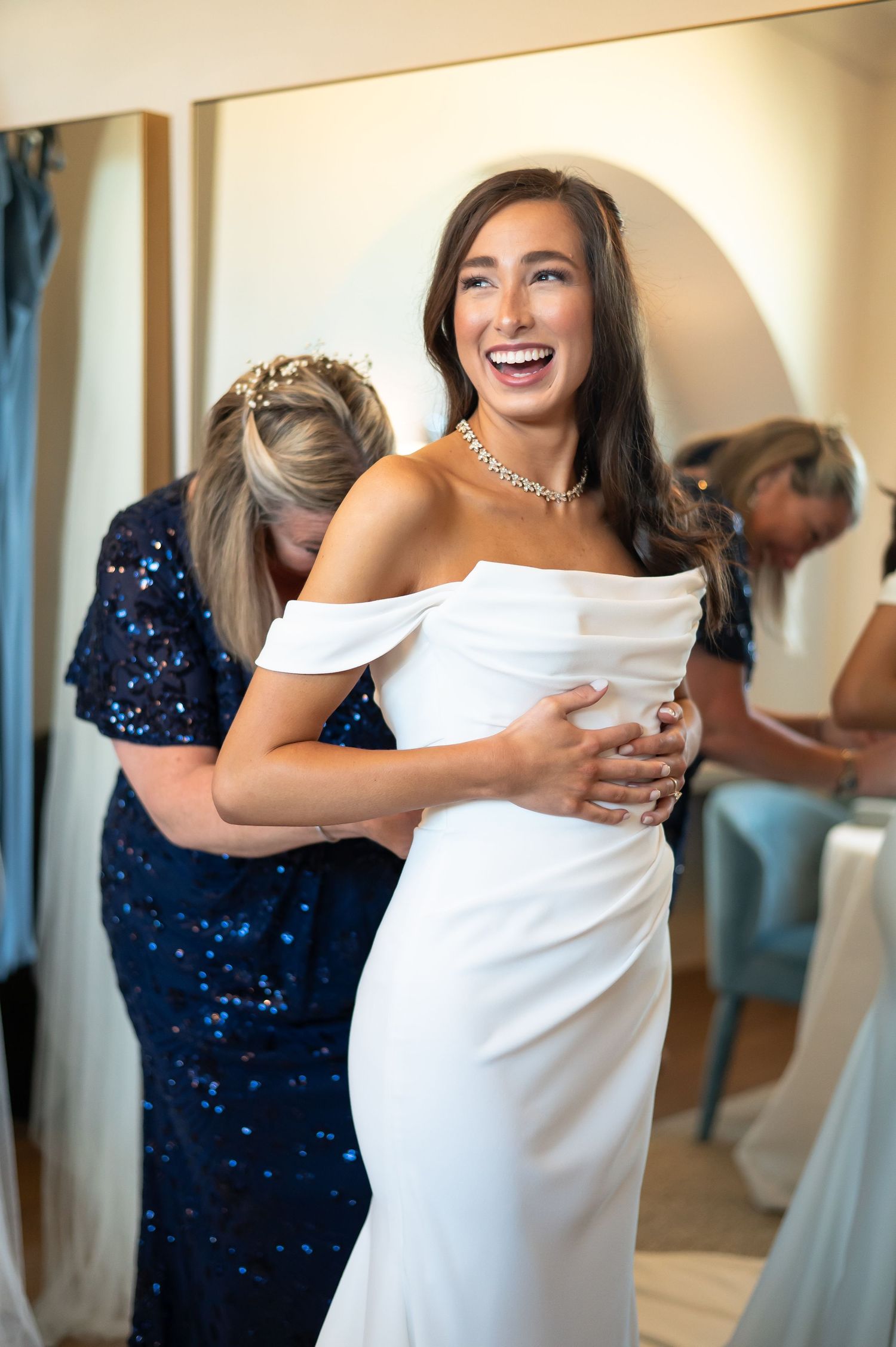 Two women in navy blue and white dresses share an emotional embrace during a wedding celebration.