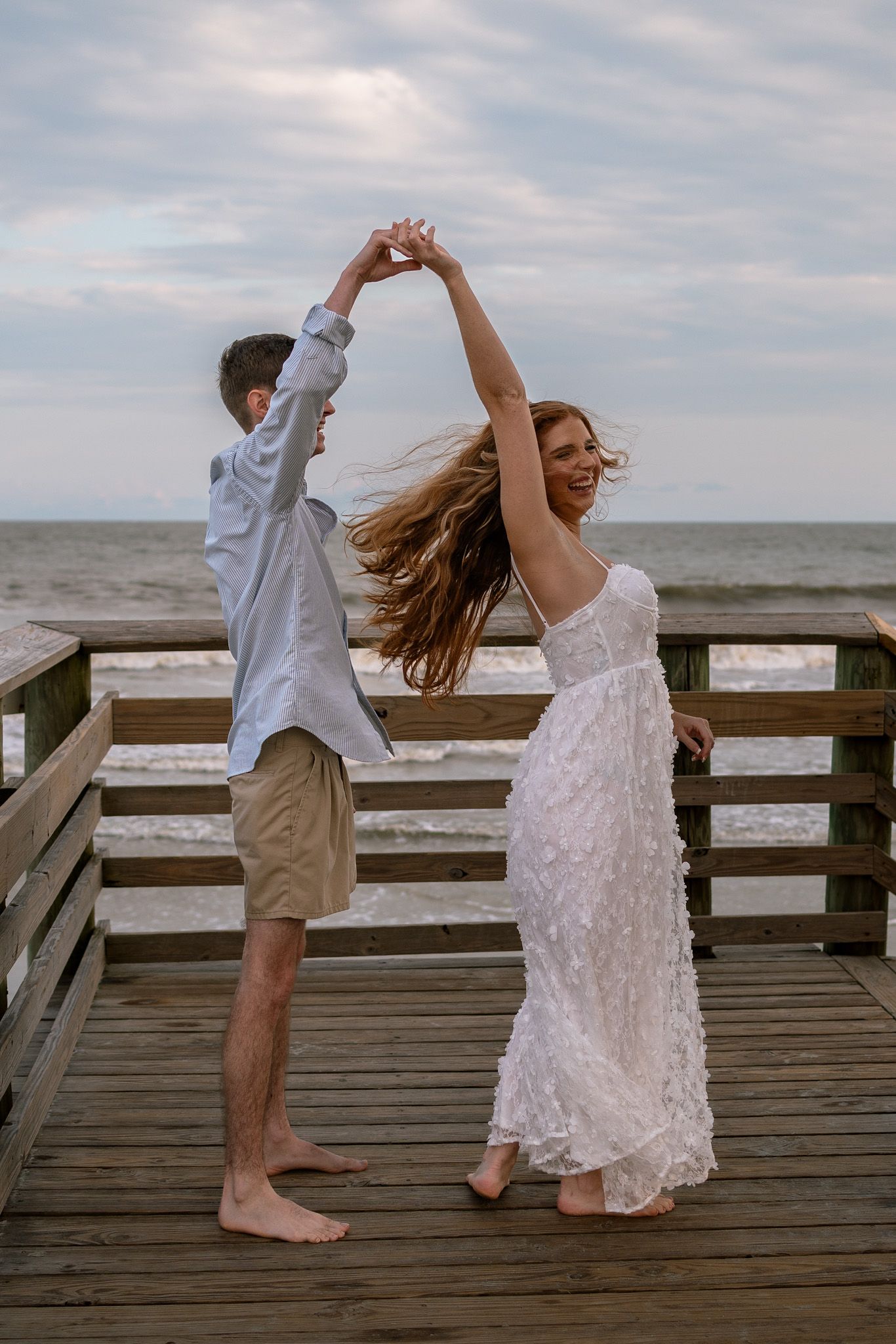 Couple dancing together on a wooden pier overlooking the ocean.