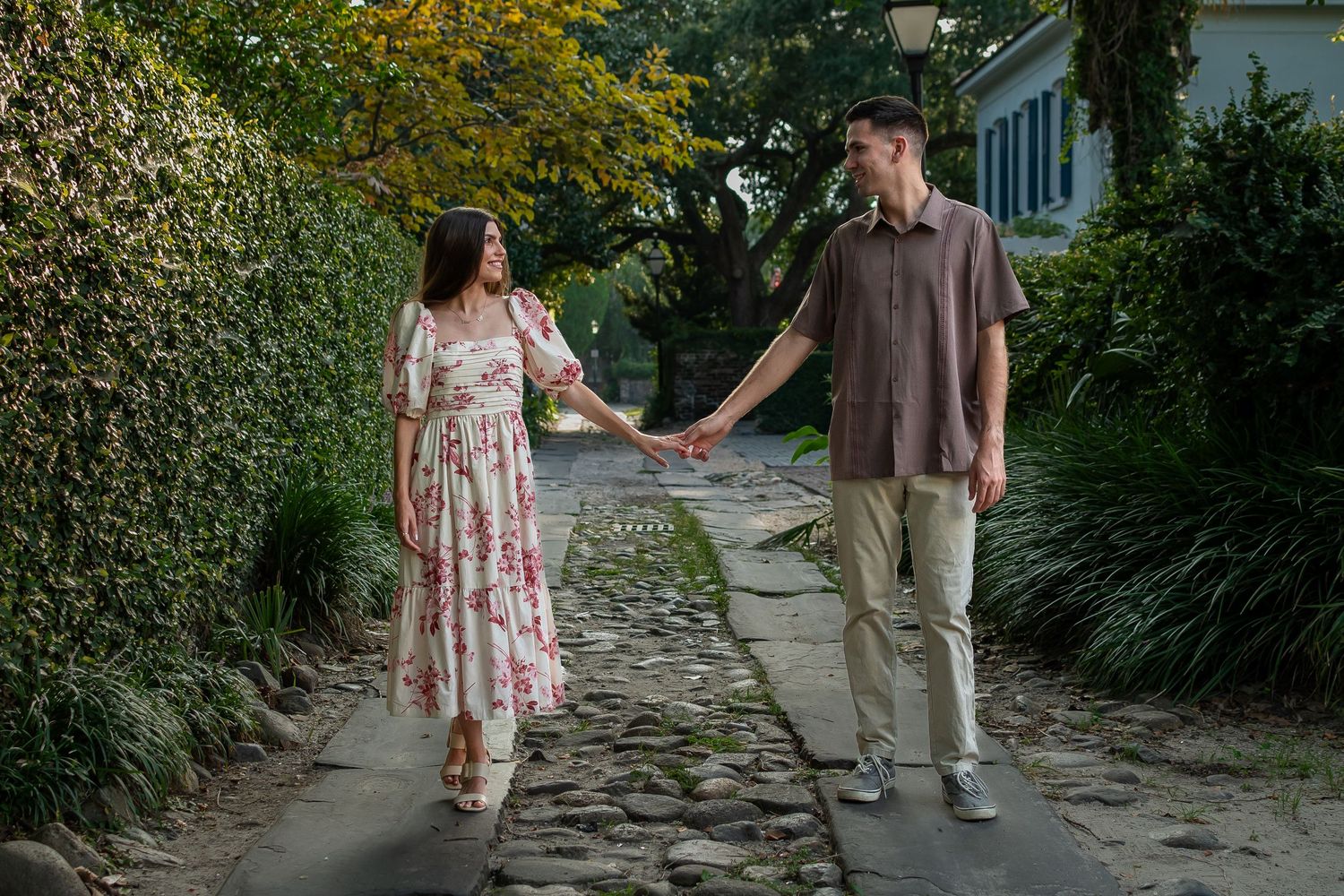 Couple walking hand in hand along a stone path surrounded by lush greenery.