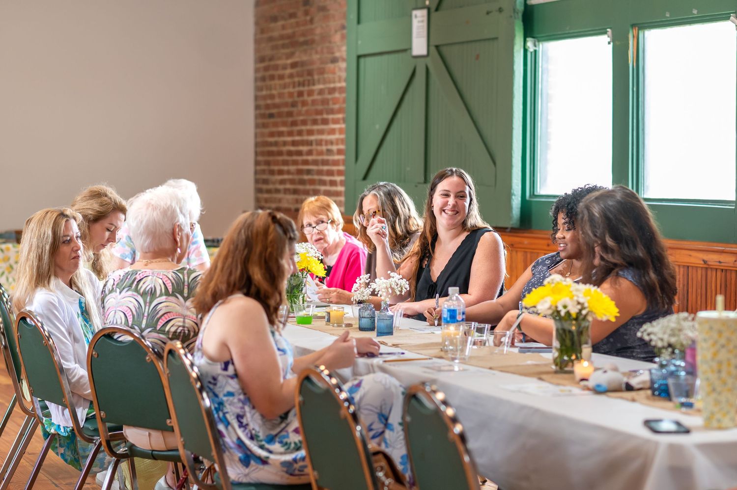 Large group gathers around long tables in a brick-walled community space for a social event.