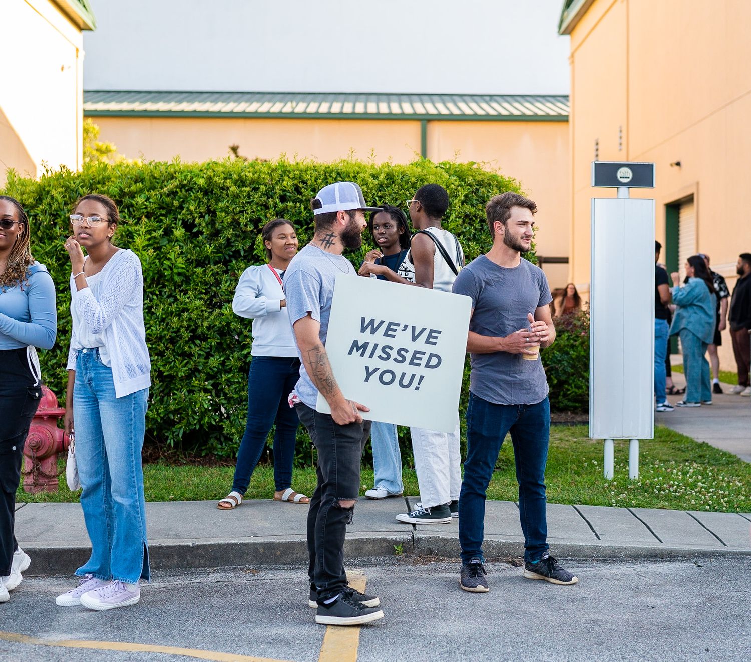 A long line of people waiting outside a building in casual attire on a sunny day.