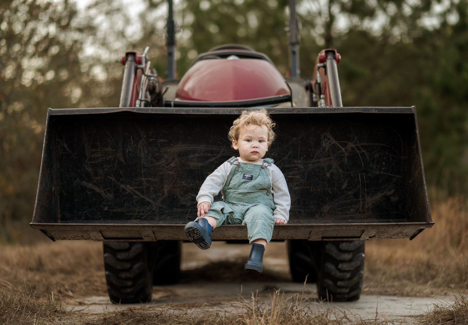 A young child sits on the back of a black pickup truck tailgate in a rustic outdoor setting.