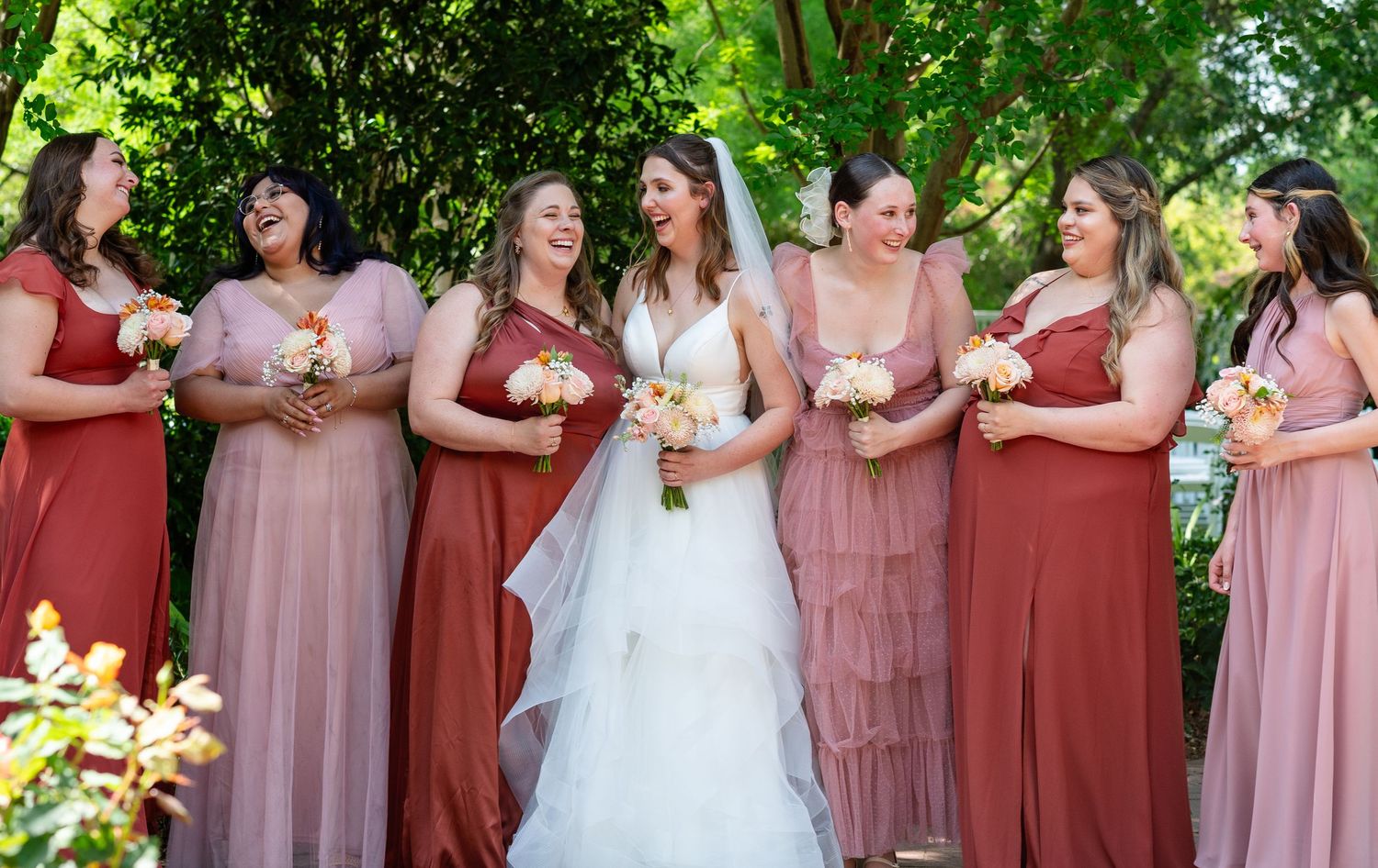 Wedding party in burgundy and pink dresses posing together outdoors.