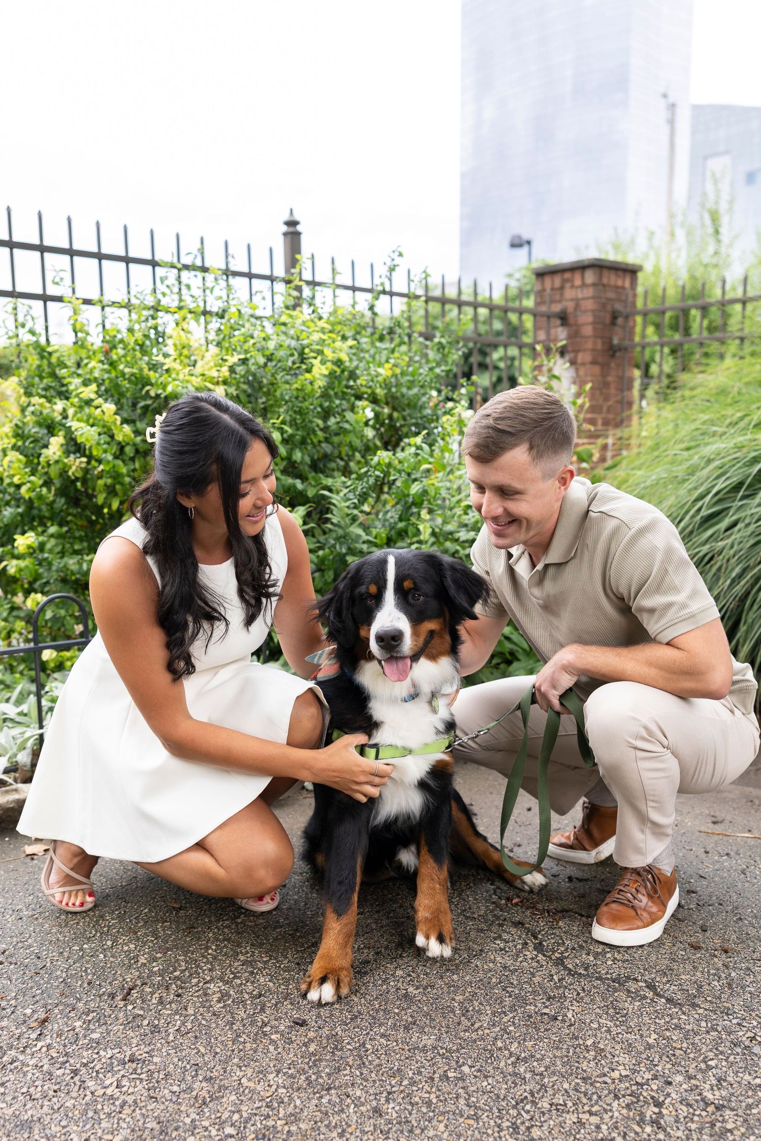 A couple sitting with their Bernese Mountain Dog on a gravel path in a garden setting.