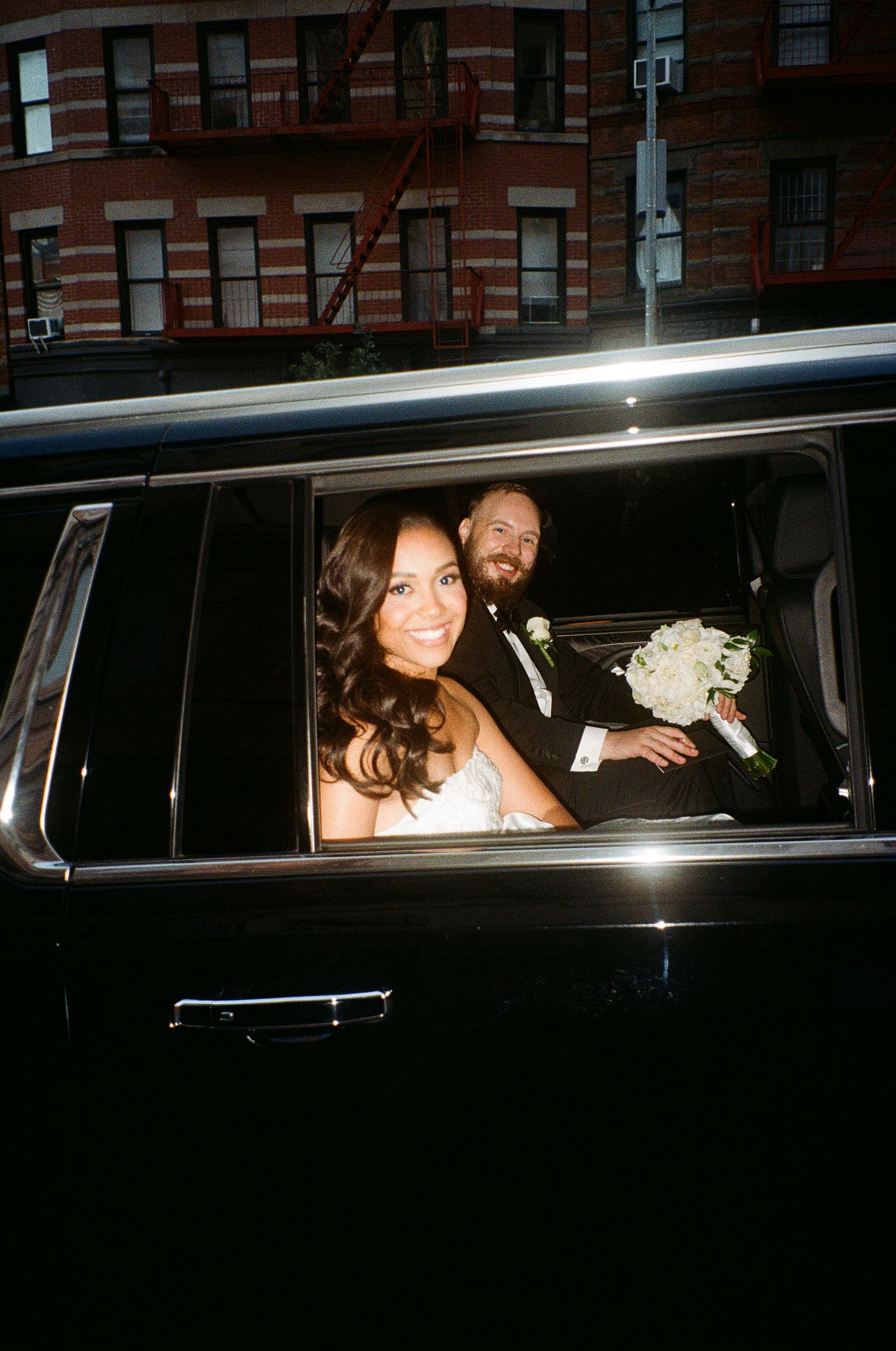 Newlyweds smile together in the back of a limousine.