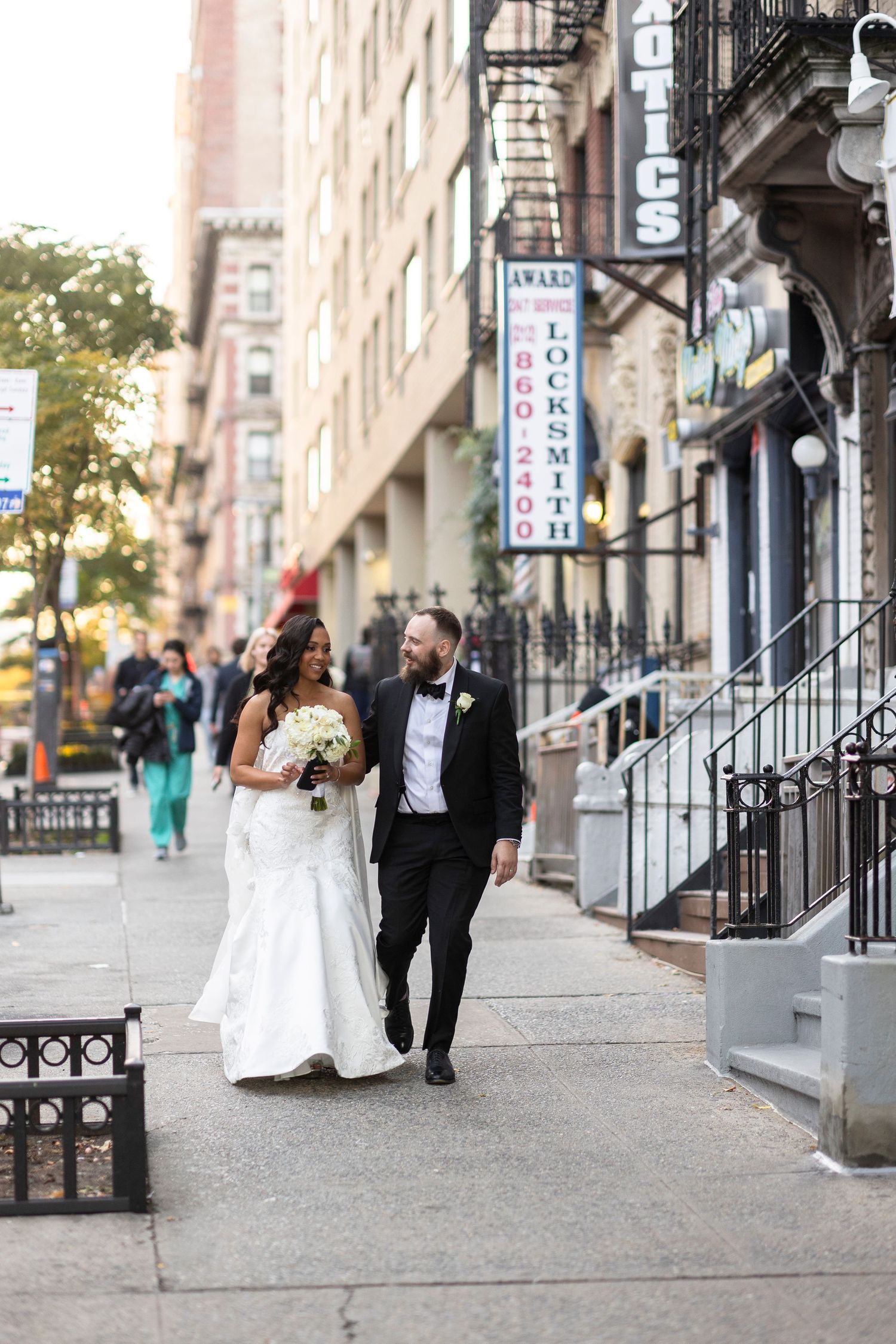 Wedding couple walking along brownstone-lined street with iron railings.