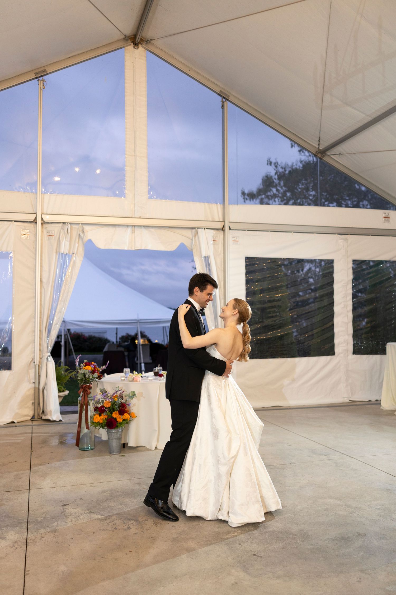 Couple dancing in a white tent venue with scenic outdoor views through the windows.