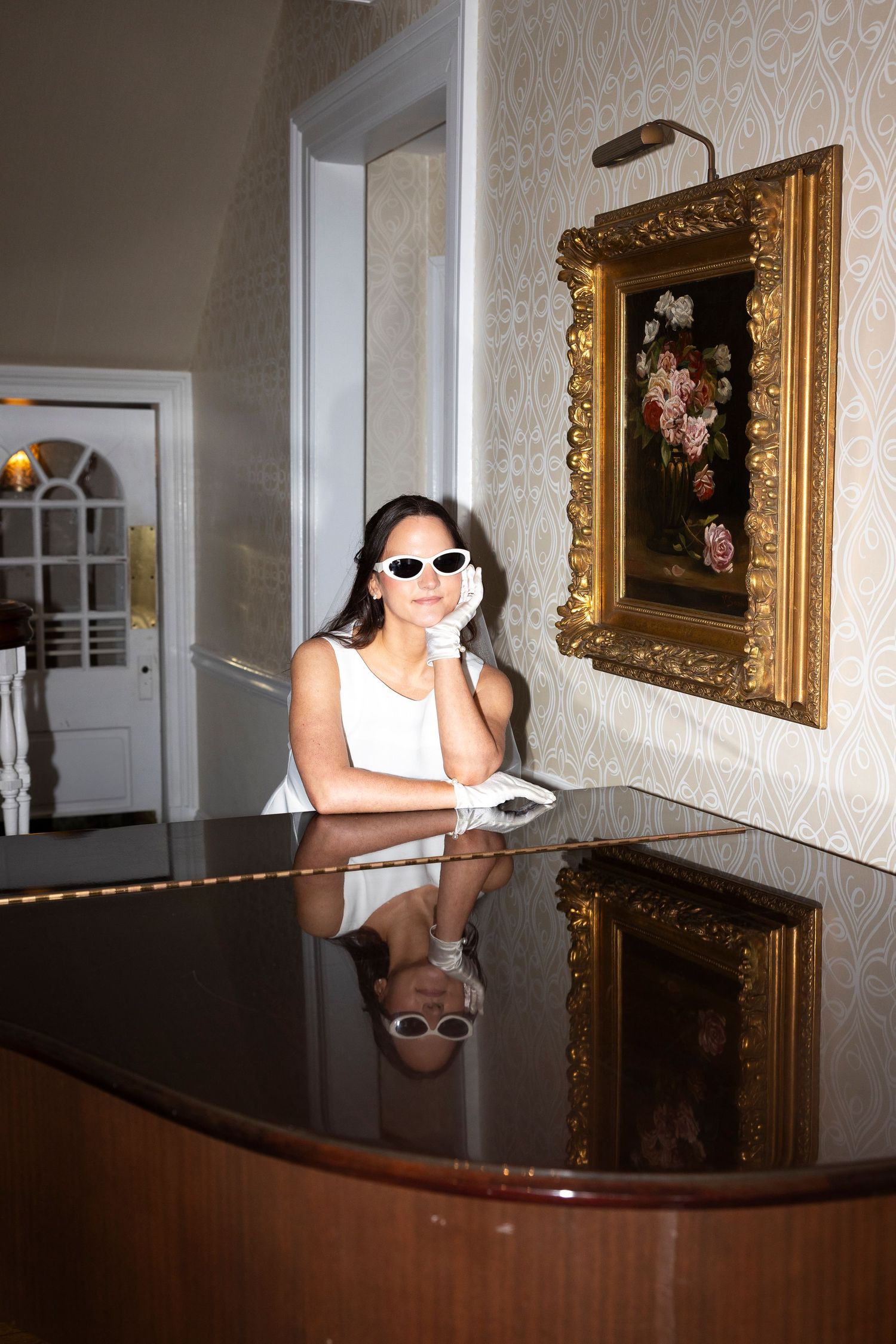 A glamorous photo at a piano with white sunglasses and a reflection in the polished surface.