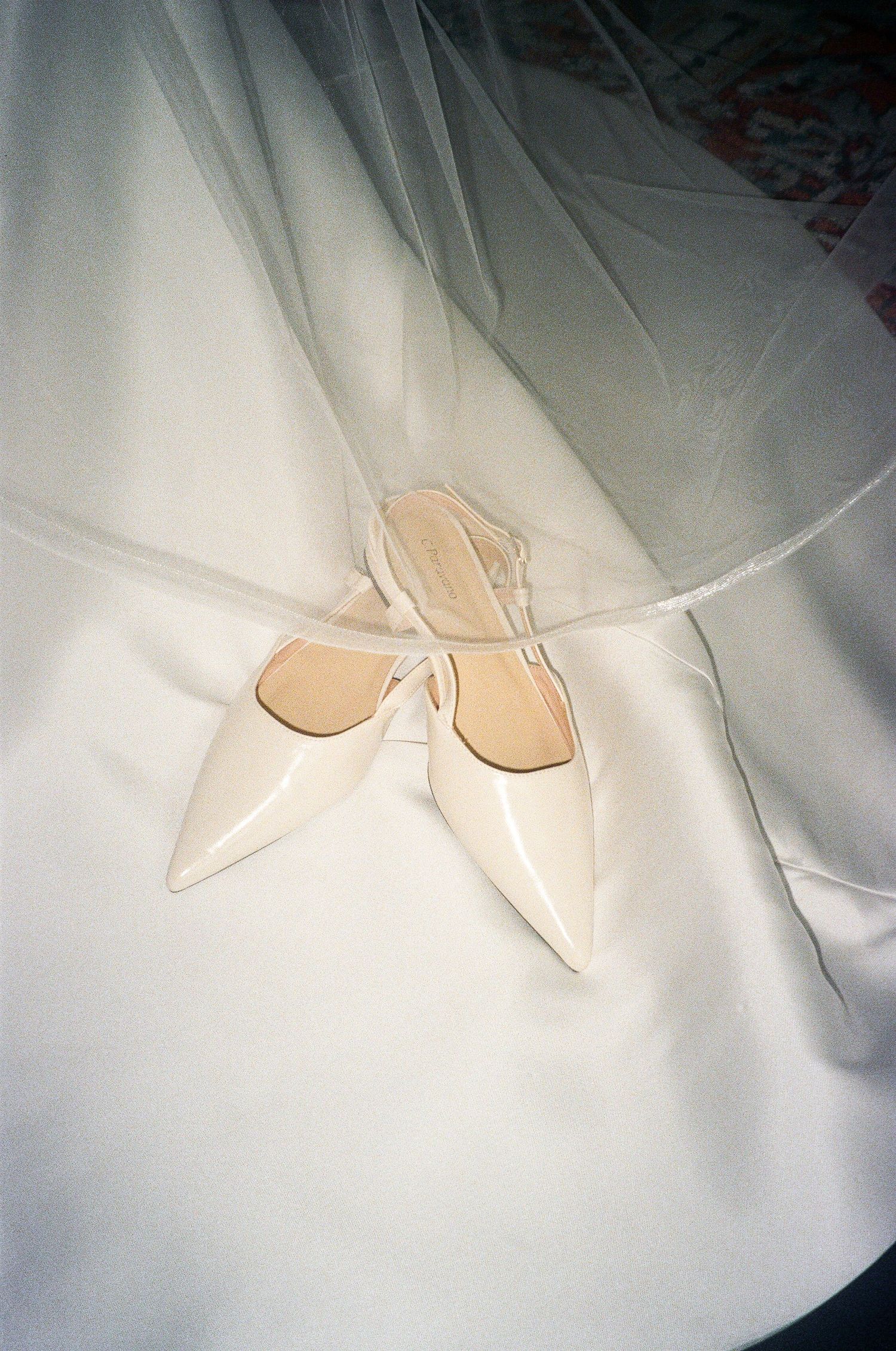 Elegant white bridal shoes photographed on flowing white fabric.
