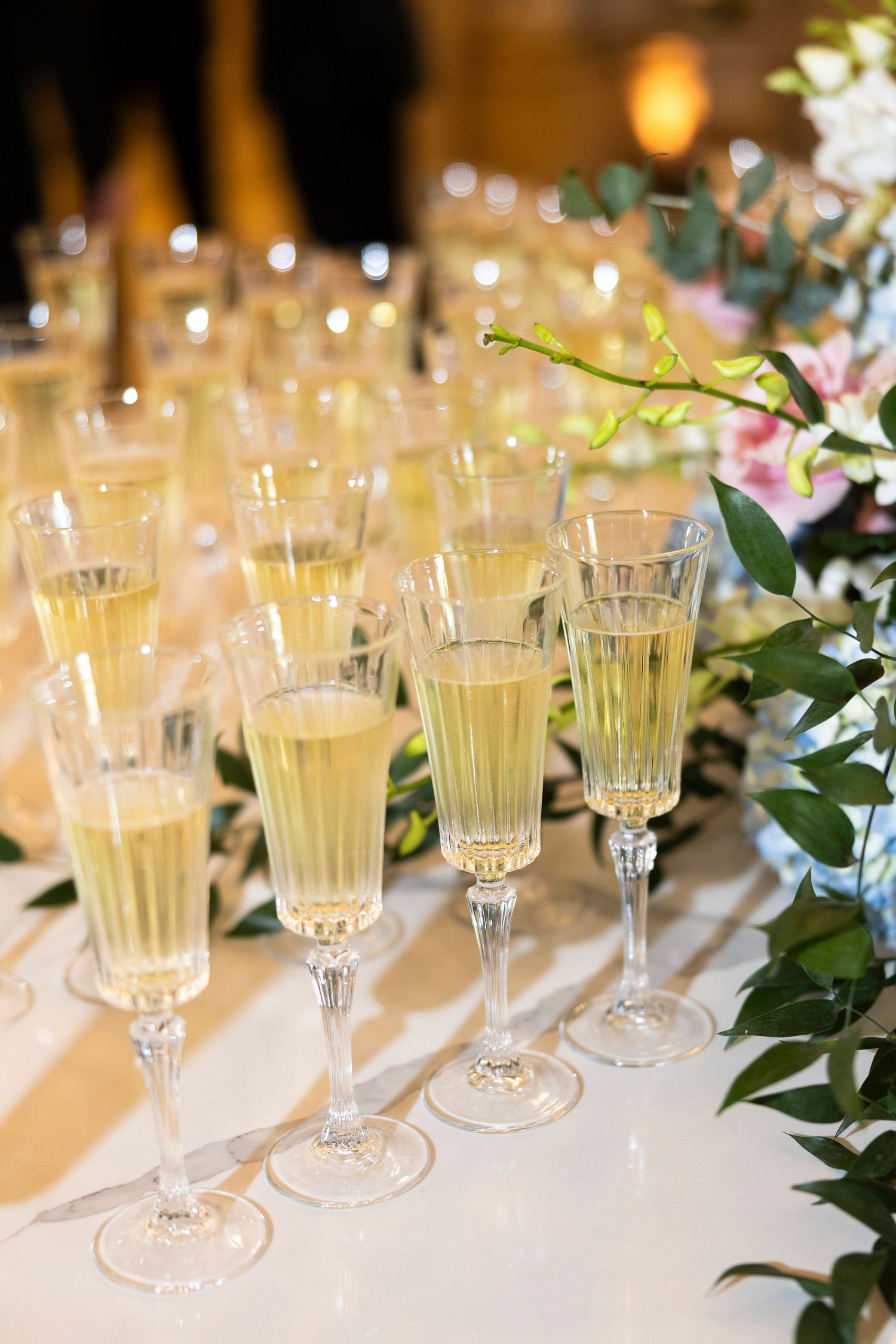 Crystal champagne flutes filled with sparkling wine arranged on a white table with floral decorations at an elegant event.