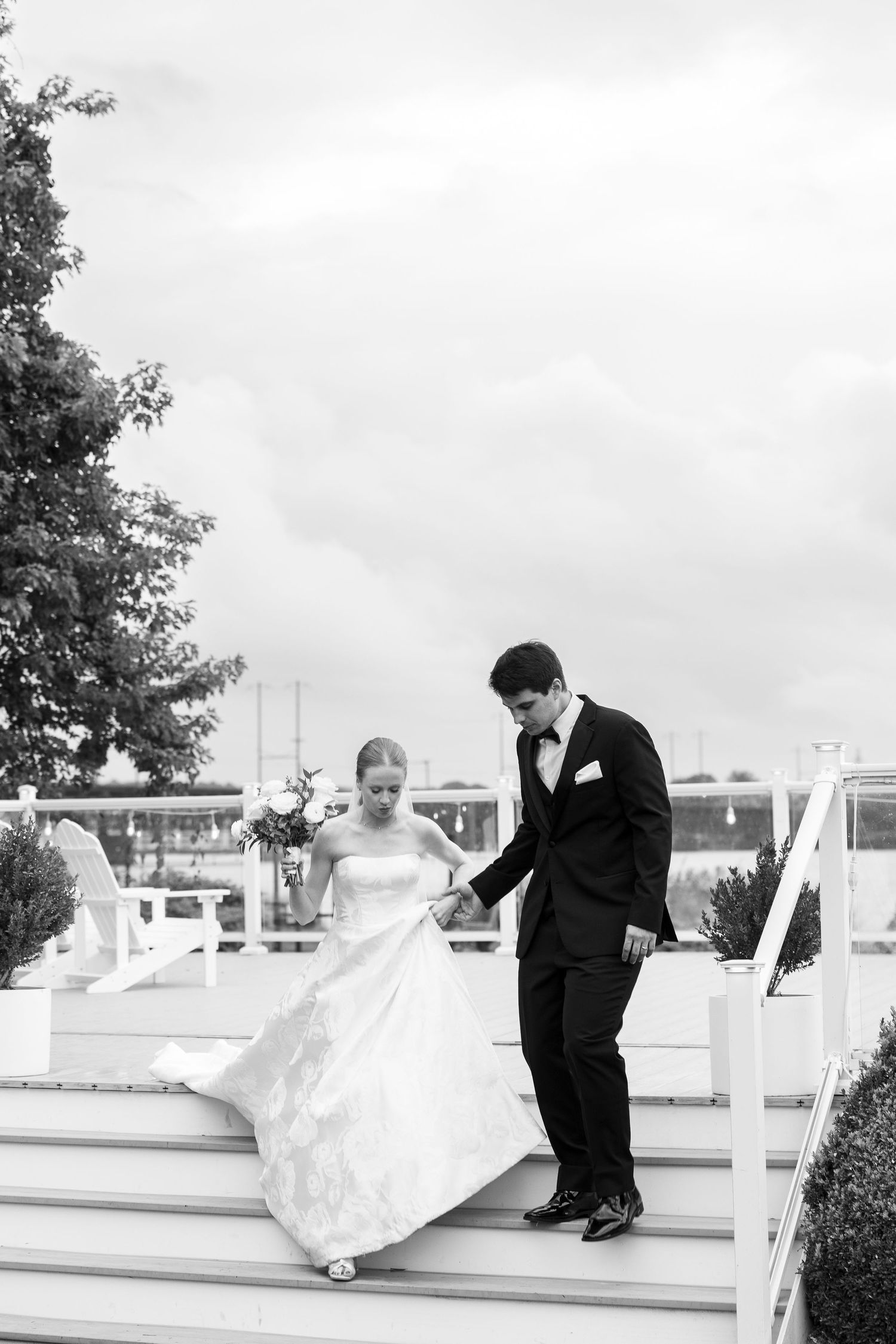 A black and white photo of newlyweds descending outdoor stairs at their waterfront wedding venue.