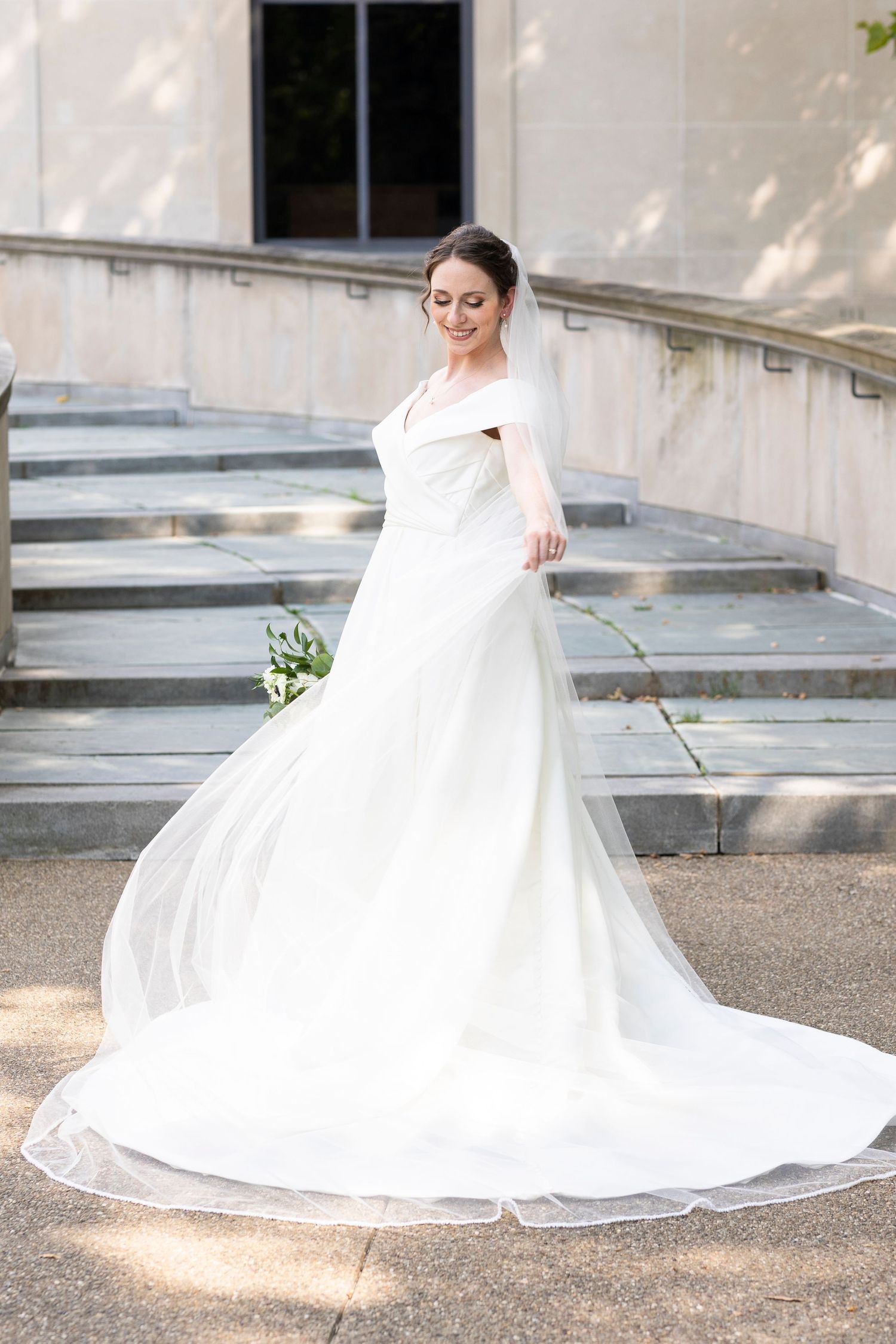 Bride in flowing white dress with train twirls on stone steps in natural lighting.