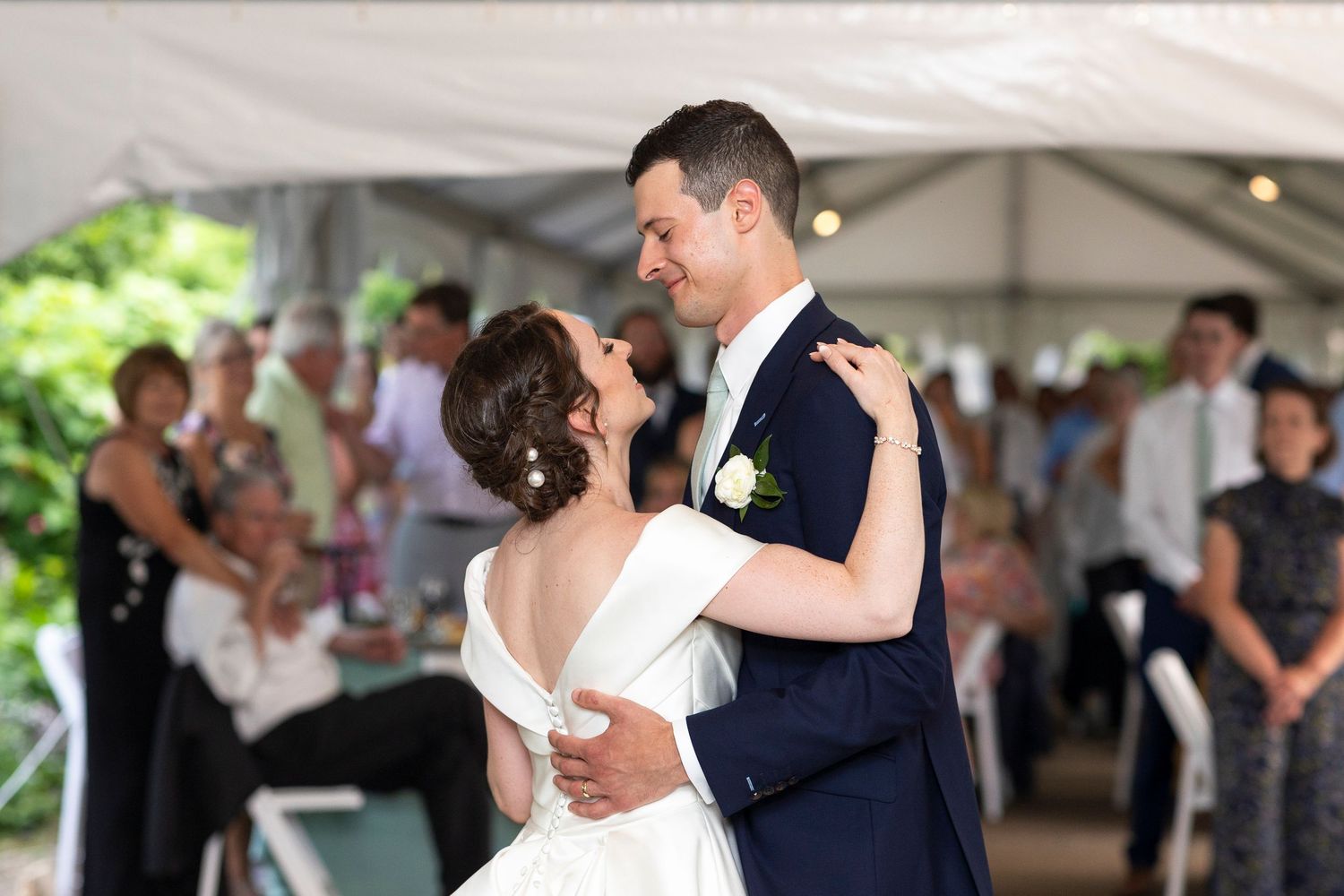 A couple dances together during their wedding reception under an outdoor tent.