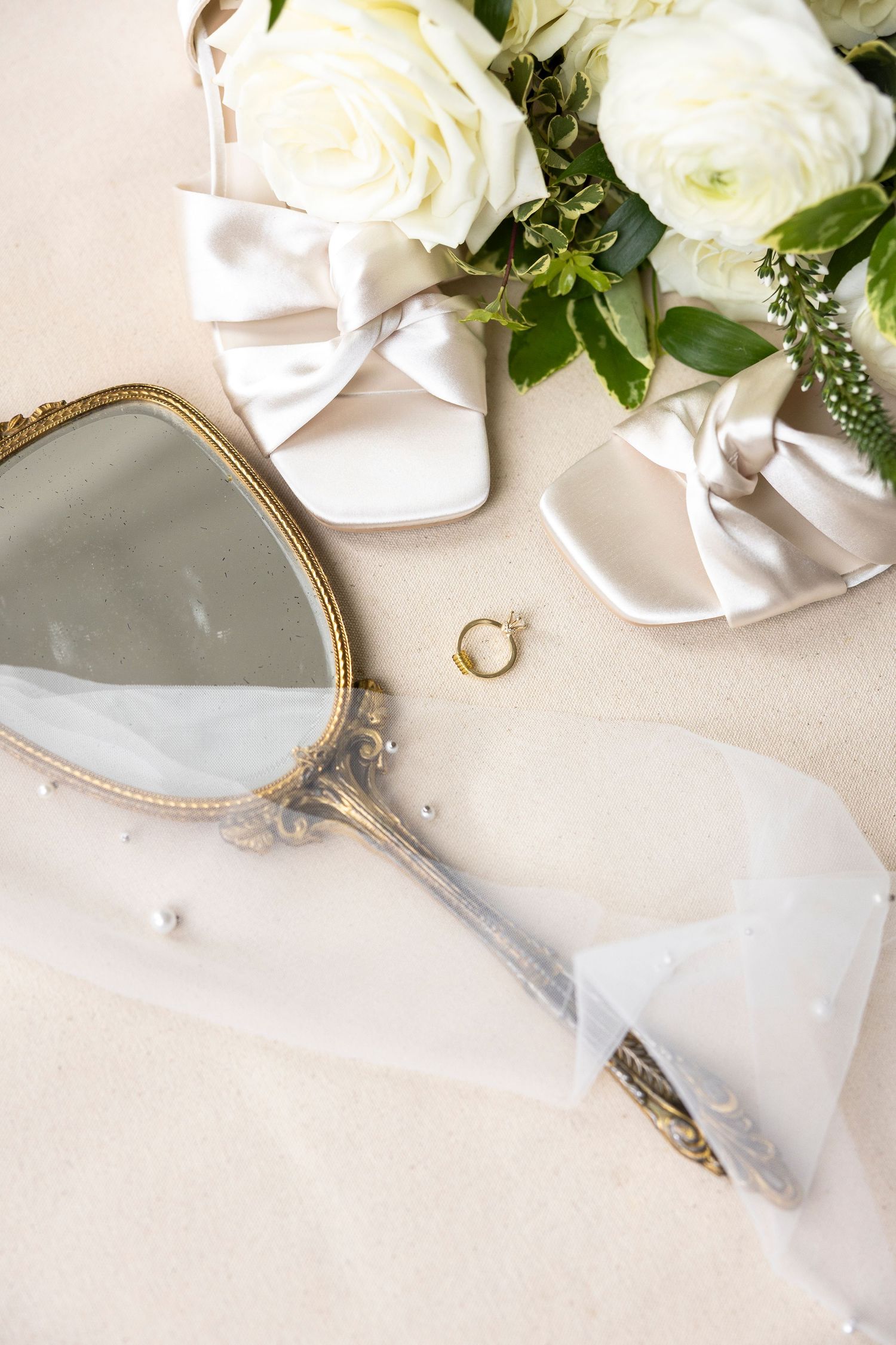Vintage hand mirror with white roses and wedding accessories on light background.