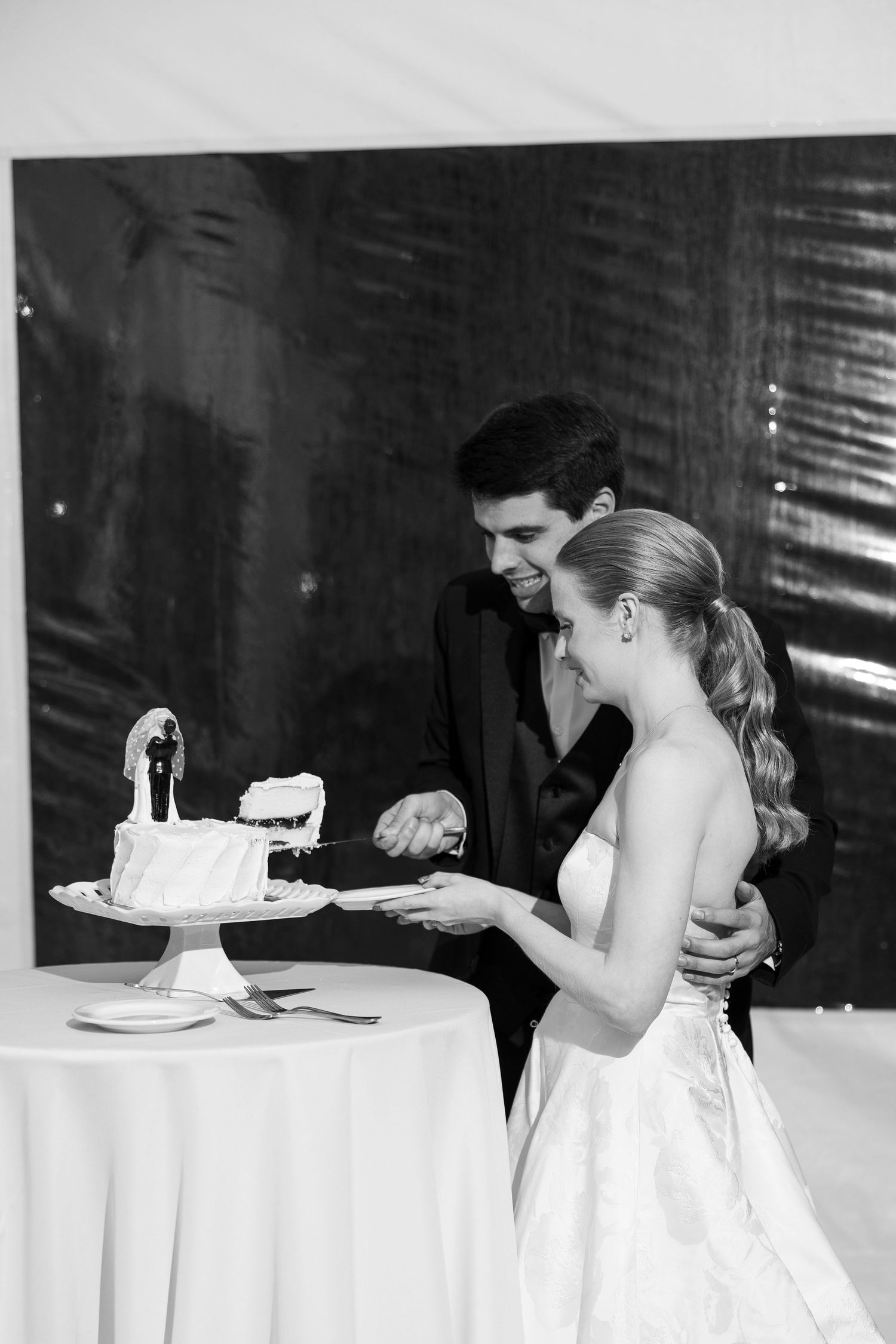 Black and white photo of wedding cake cutting ceremony at reception.