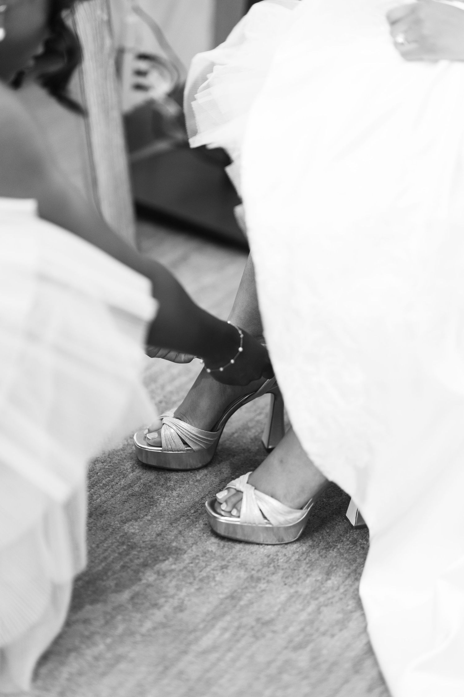 Close-up of silver wedding shoes against white dress hem on grey carpet.