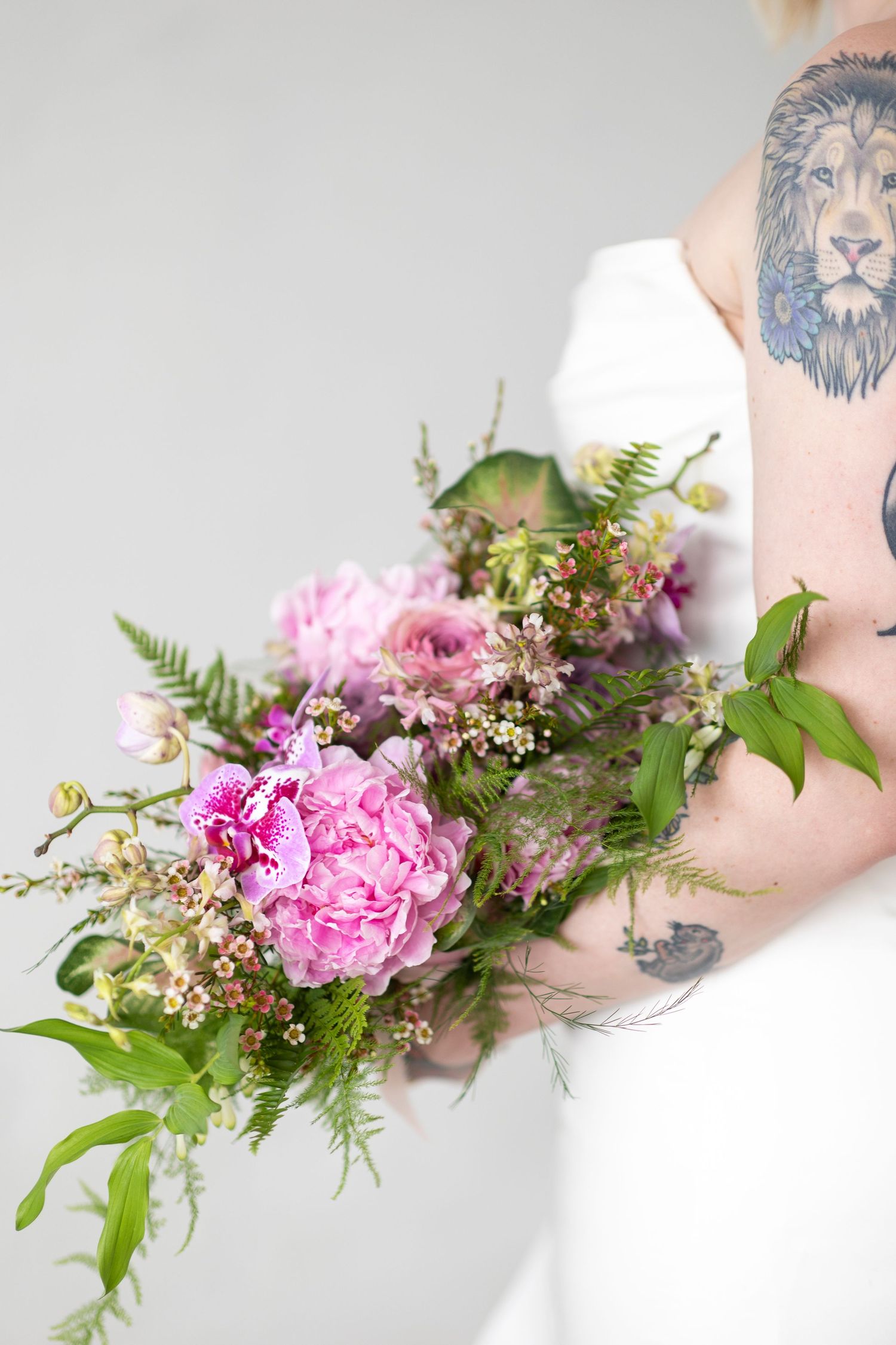 Pink and purple floral arrangement with ferns and greenery on white background.