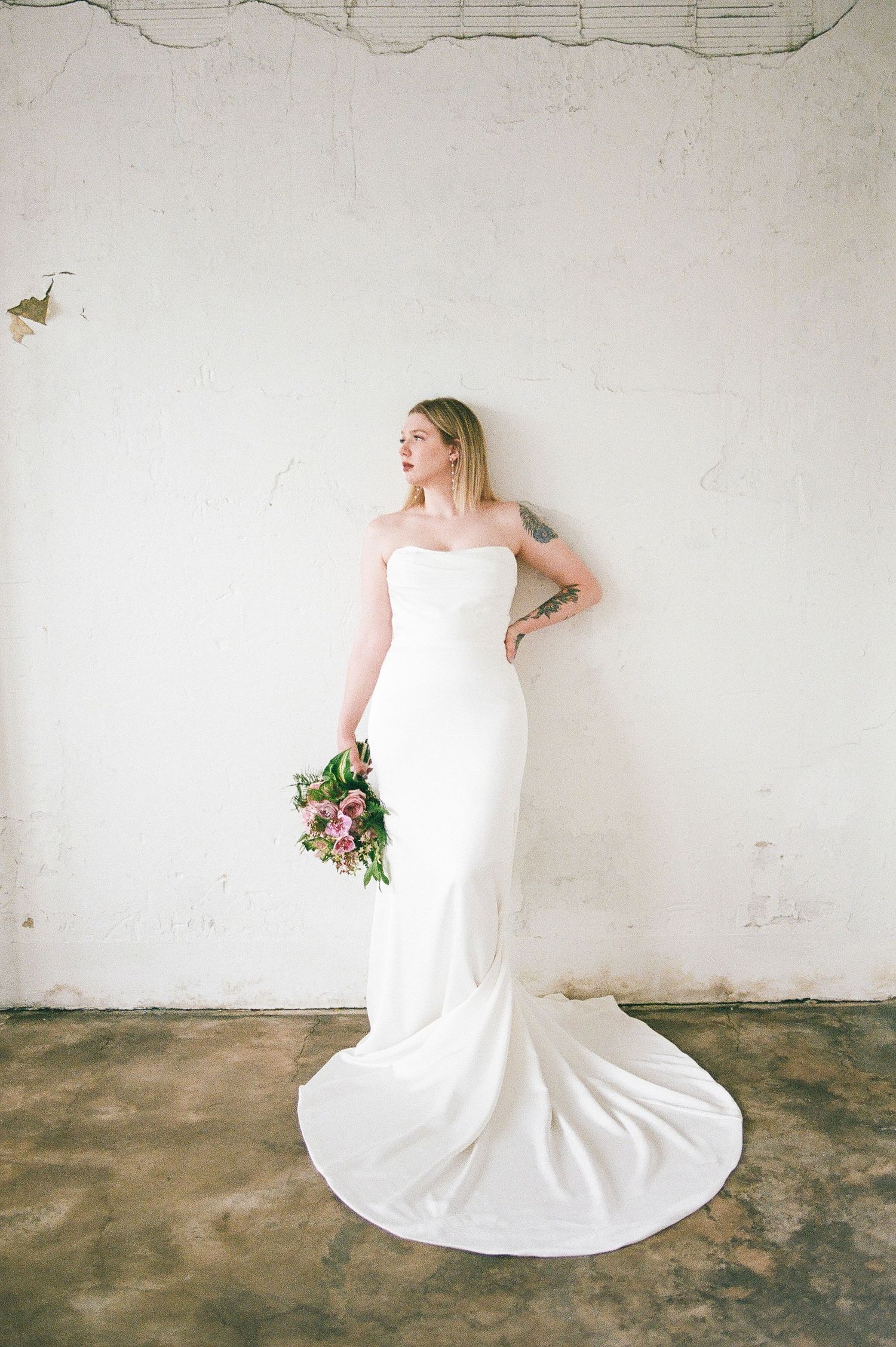 Flowing white wedding dress with dramatic train photographed against rustic concrete floor.