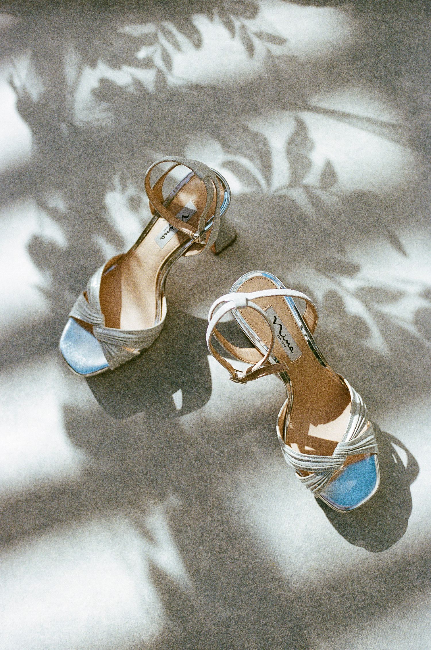 Elegant silver wedding shoes with blue accents casting artistic shadows.