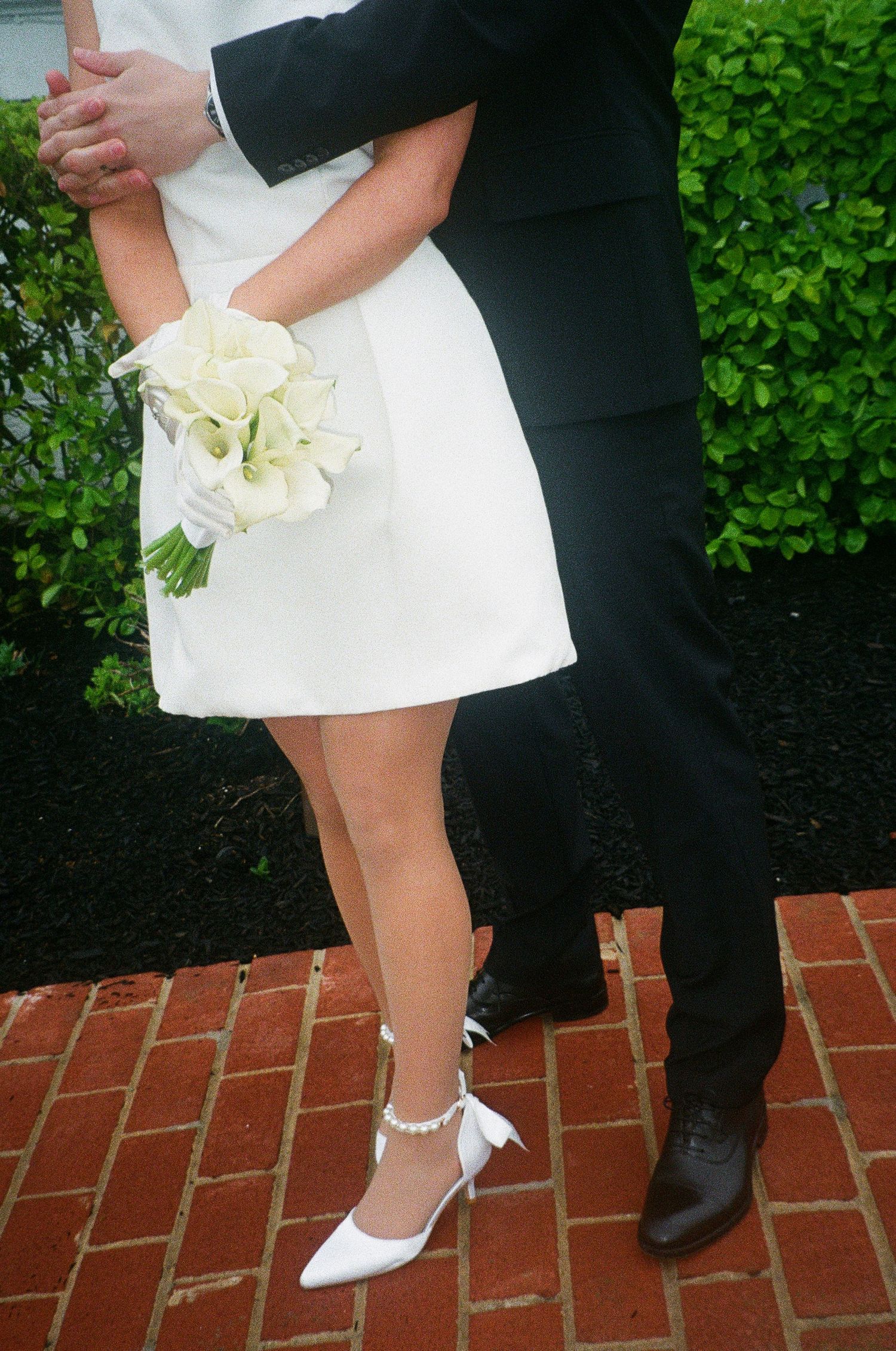 A close-up of formal wedding attire showing a white dress, black suit, and white bouquet.